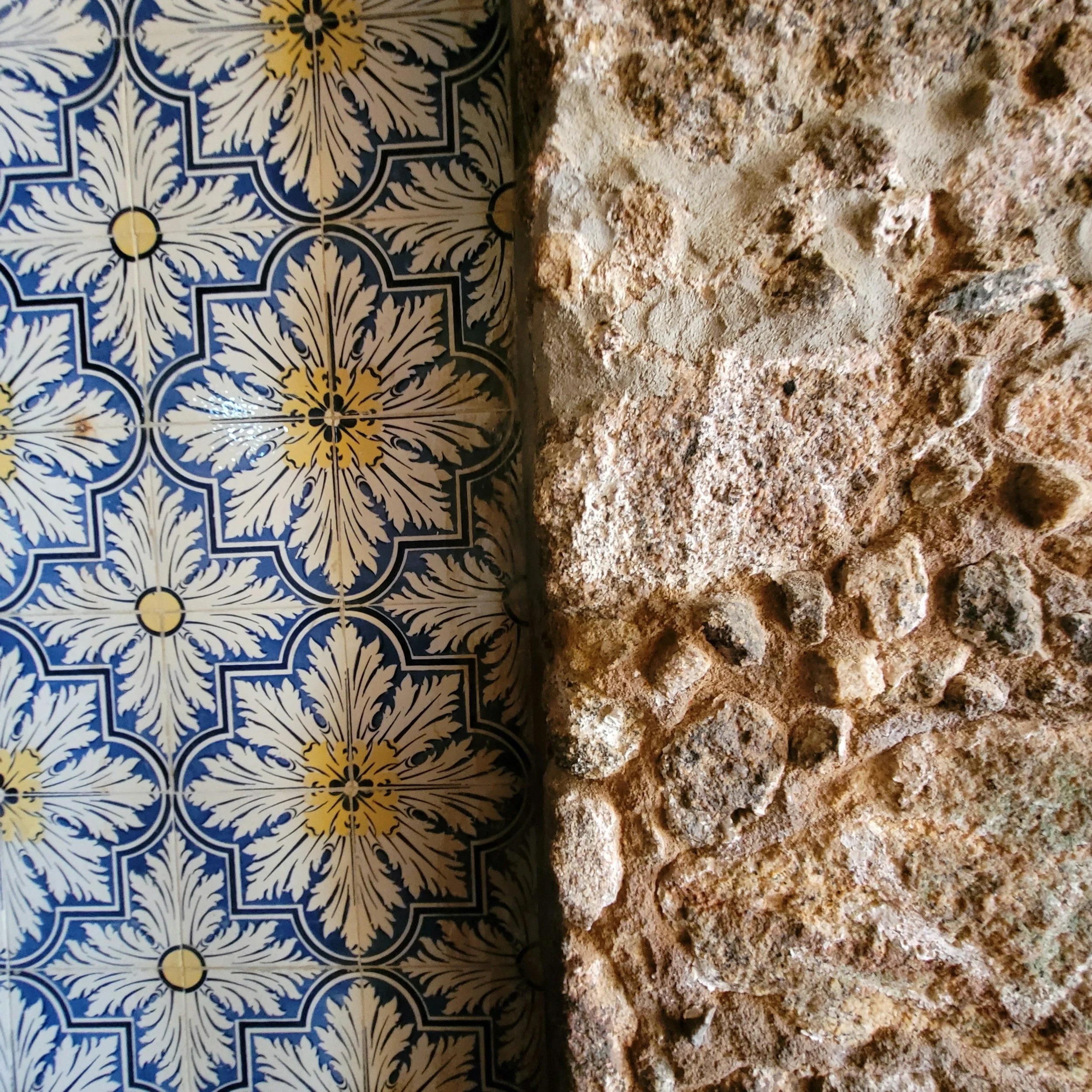 Close-up of ornate blue, white, and yellow patterned tile next to a beige and brown speckled granite countertop.