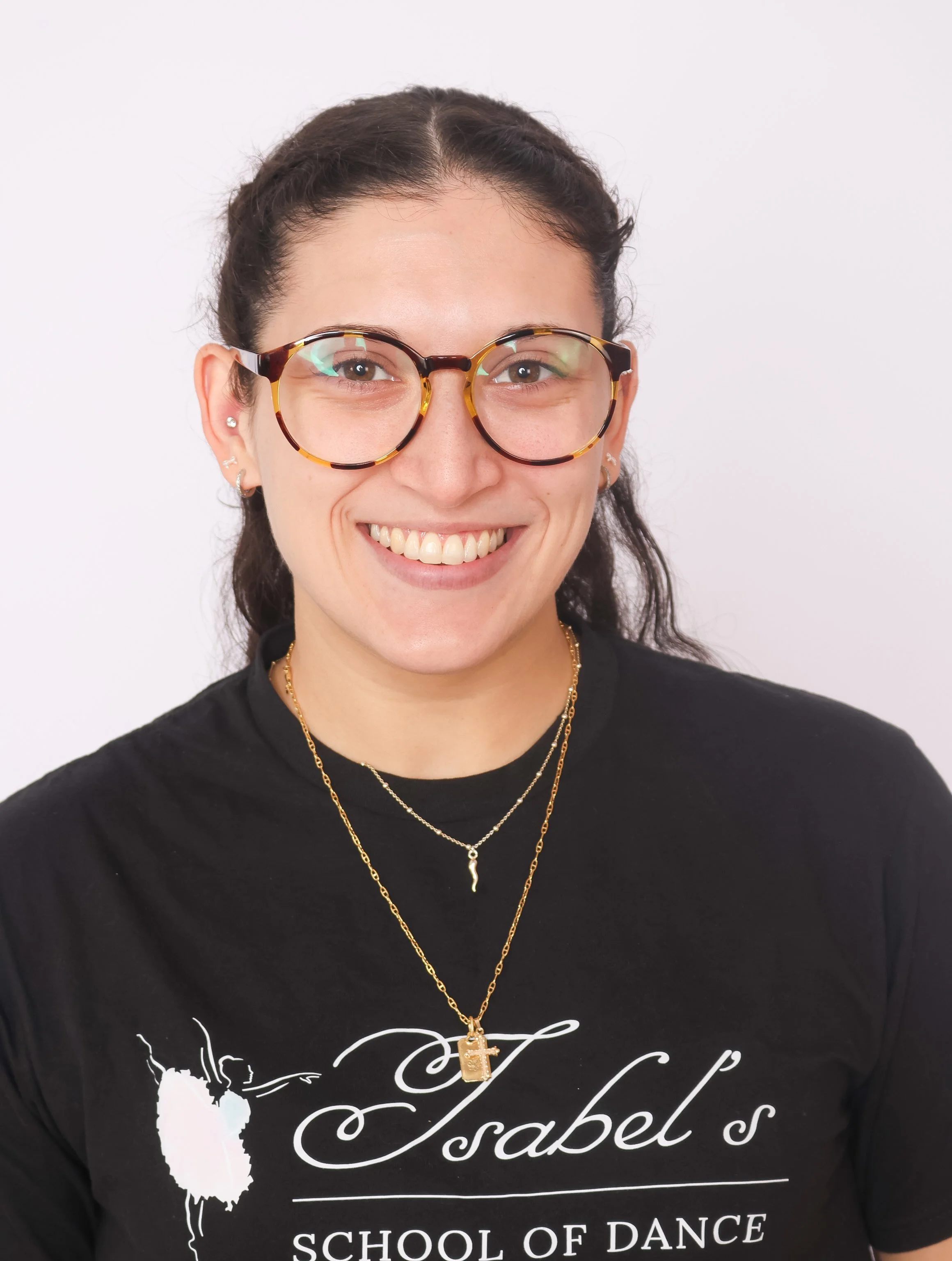 Smiling woman with long brown hair taking a selfie indoors with stairs and window in the background.
