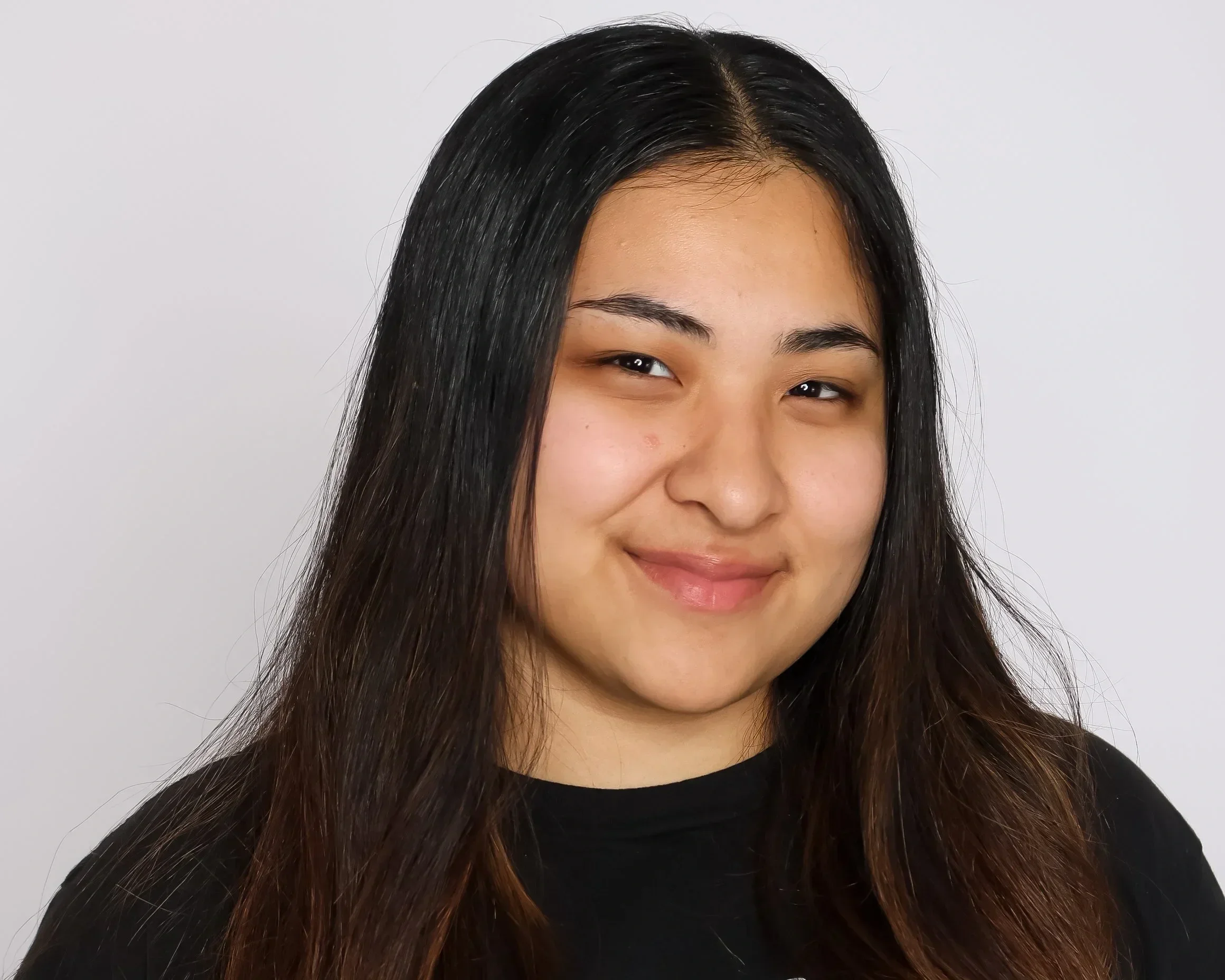Close-up portrait of a young woman with long dark hair, smiling softly with a neutral background.