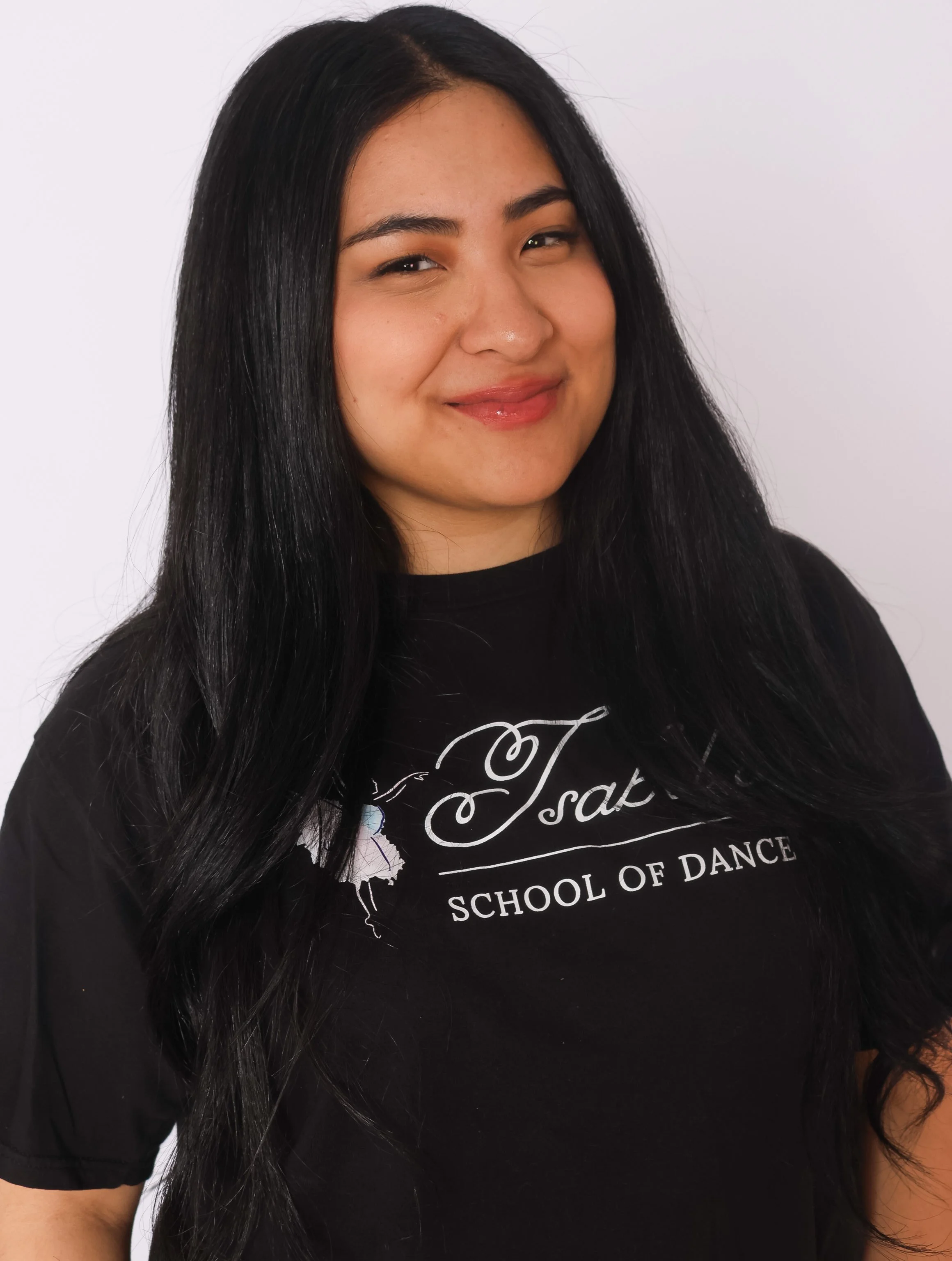 Close-up portrait of a young woman with long dark hair, smiling softly with a neutral background.
