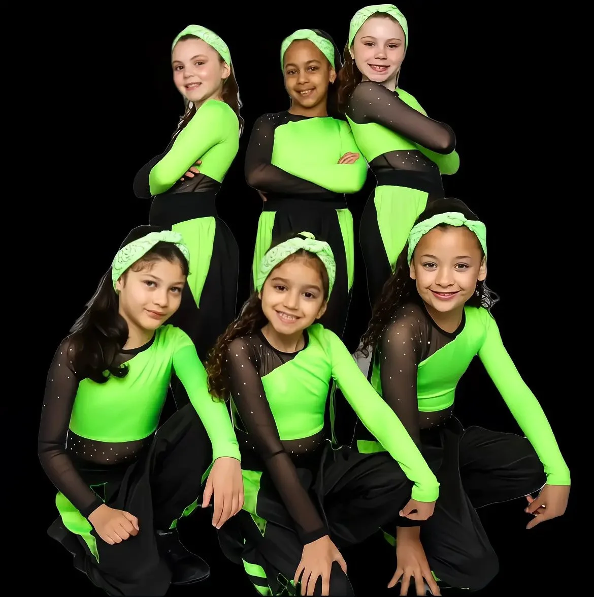 Group of seven young girls in matching neon green and black dance costumes posing against a black background.