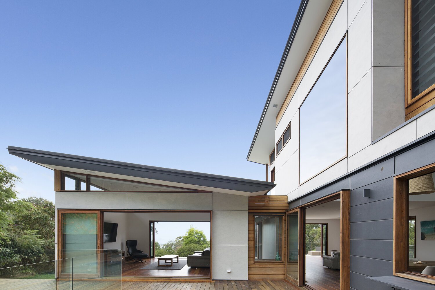 Exterior view of various custom made timber window and doors, including a large multi-panel sliding glazed timber door, slide over wall doors and louvered and fixed windows.