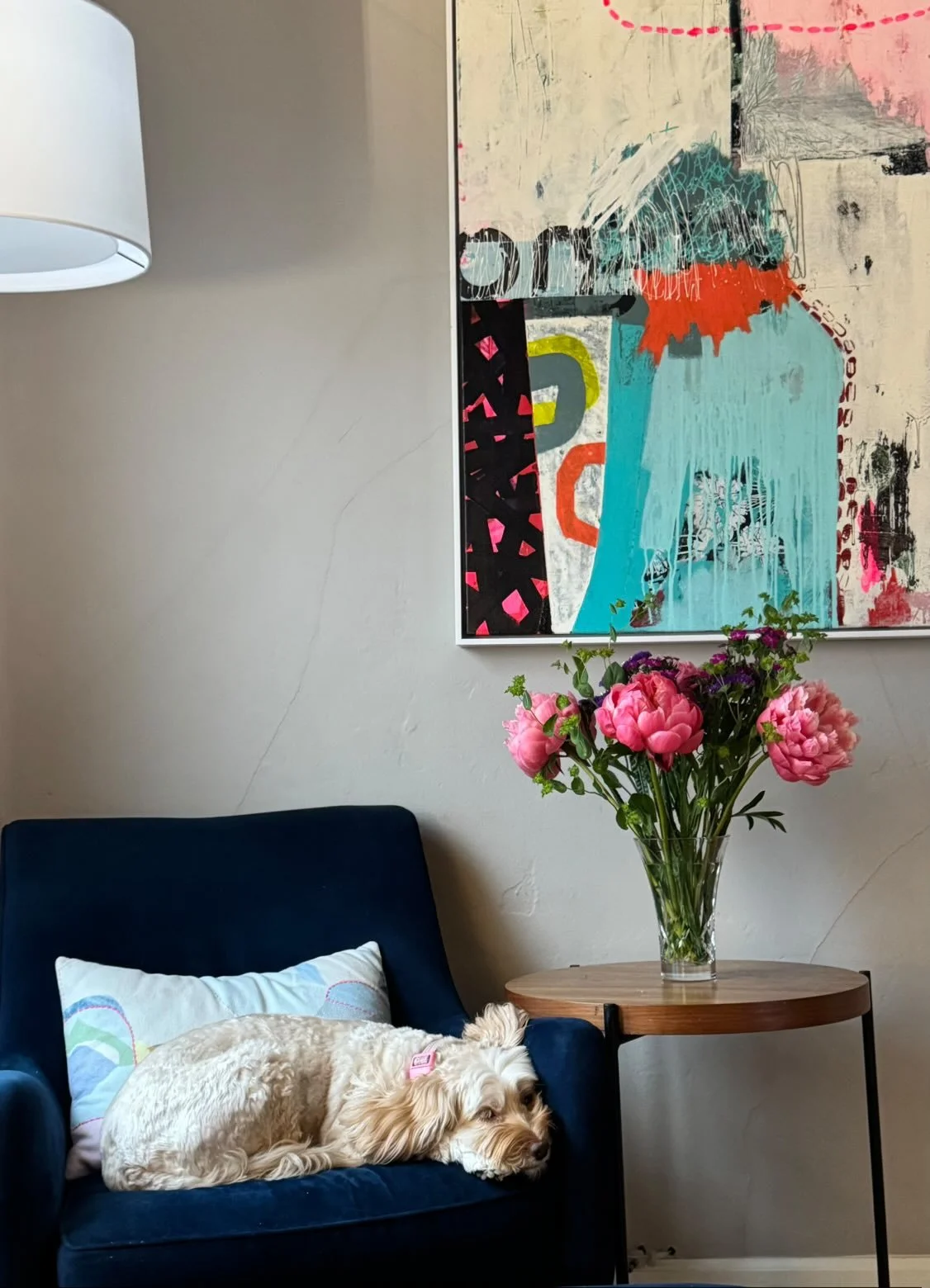 An abstract colorful painting with a combination of pink, white, black, blue, red, yellow, and gray colors, hung on a beige wall.