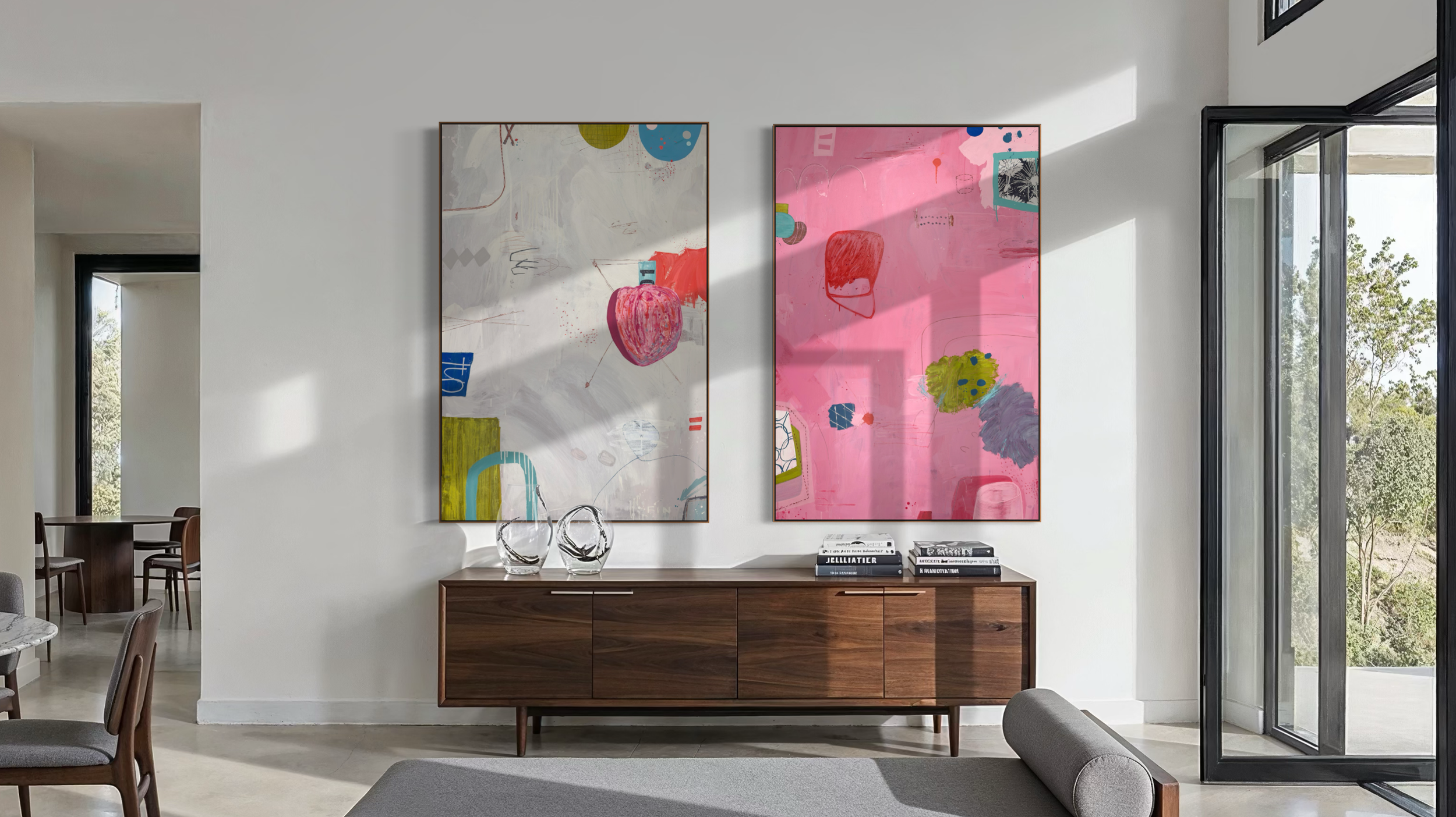 A modern living room with two large abstract paintings on the wall, a wooden sideboard, two glass vases, and a stack of books, with natural light coming in through windows.