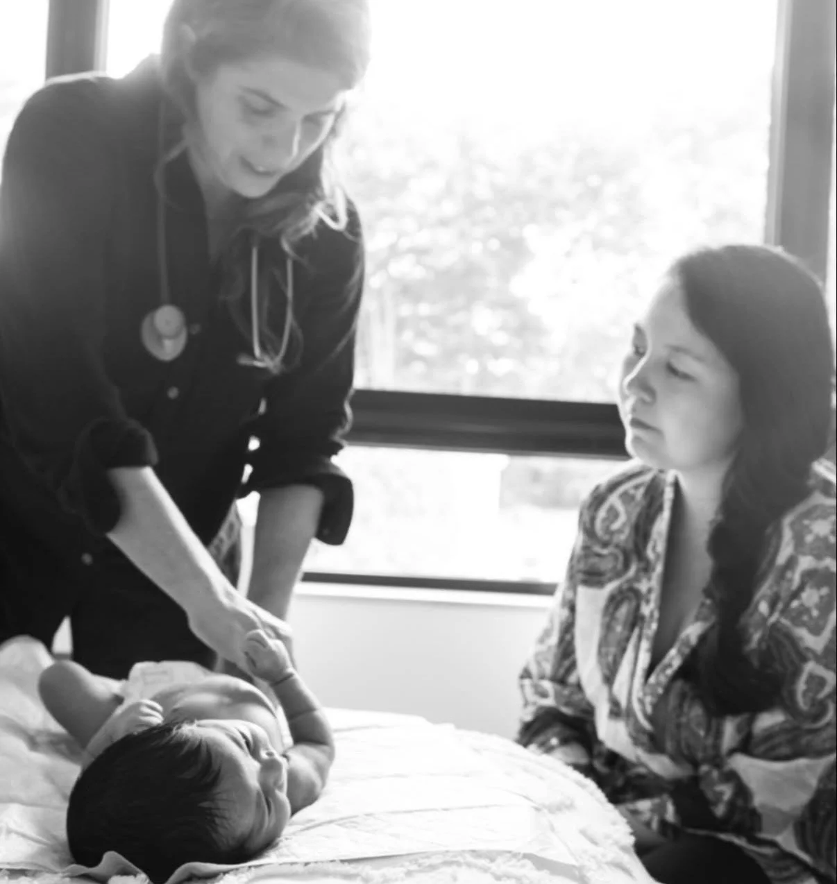Eva Zasloff, MD, examining a newborn on a bed during a home visit while the mother looks on. Black-and-white photograph.