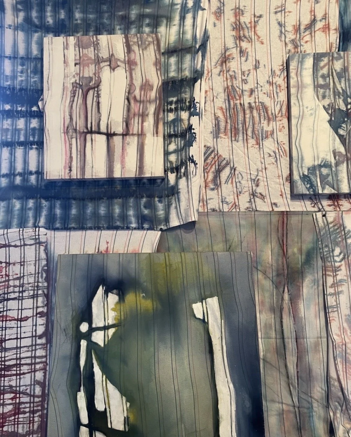 Birth Story series by Eva Zasloff: hospital receiving blankets painted with natural and synthetic pigments, layered and overlapping on a wall, their woven stripes showing through washes of blue, red, green and grey.