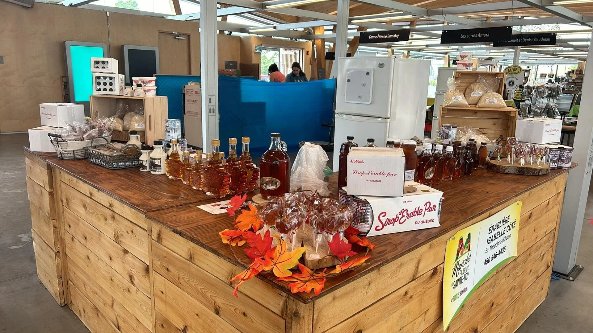 Kiosque de vente de sirop d'érable avec bouteilles de sirop et décorations de feuilles d'automne dans un marché à Québec couvert.