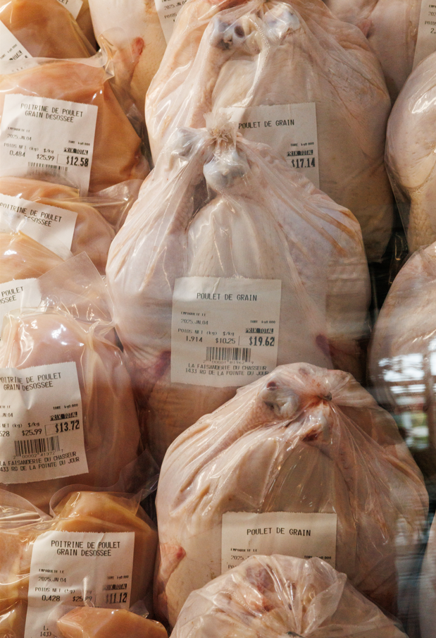 Sacs de poulet entier en plastique dans une vitrine avec des étiquettes en français.