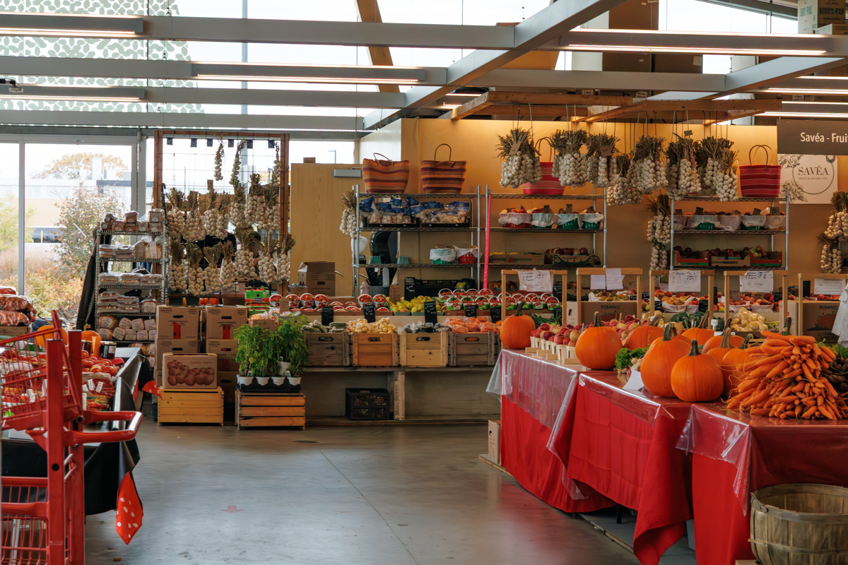 Marché de fruits et légumes avec des courges, carottes, ail, et autres produits agricoles exposés sur des tables couvertes de nappes rouges et des étagères en arrière-plan.