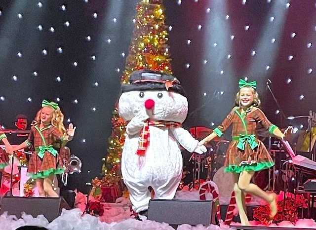 Actor in snowman costume and dancers performing on stage for a Christmas show