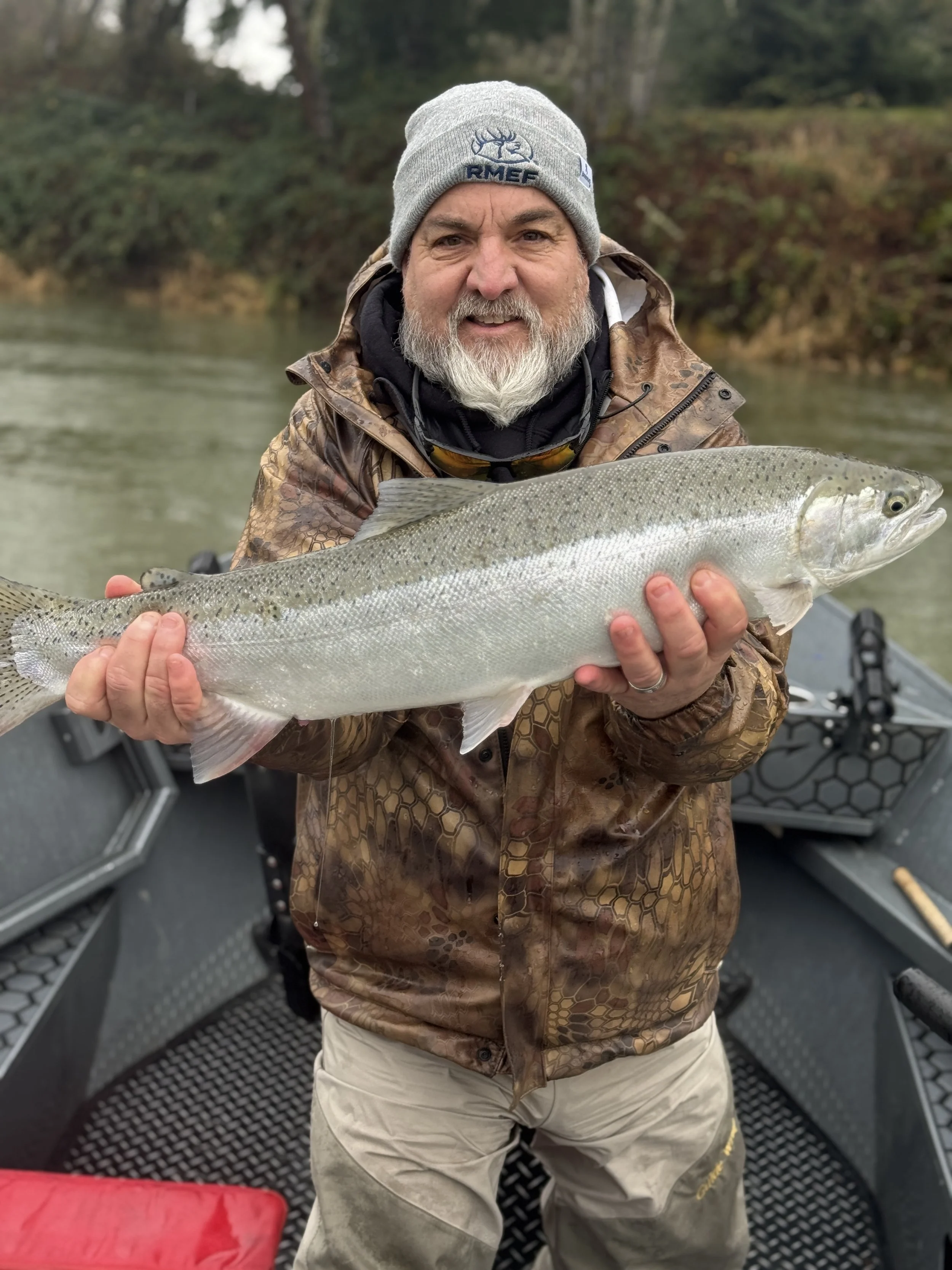 A man with a gray beard and gray beanie hat holding a large fish on a boat.