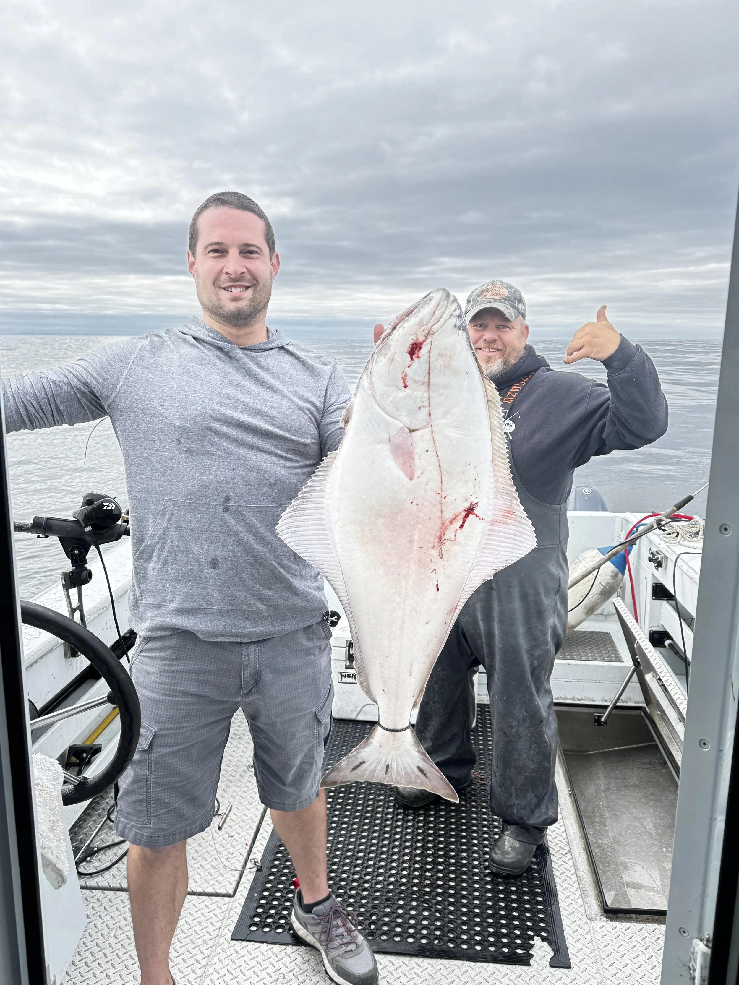 Two men holding a large fish on a boat offshore on a cloudy day.