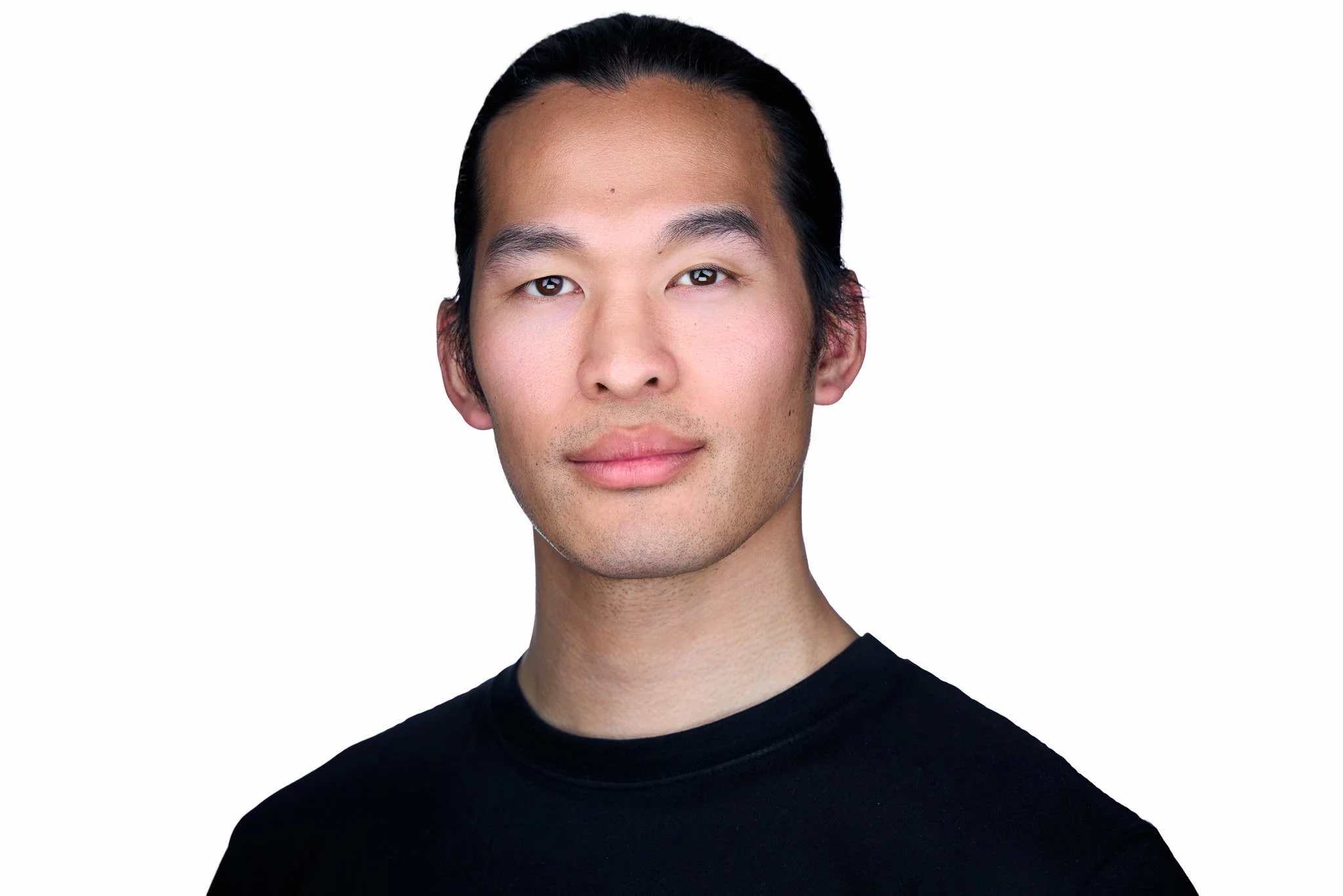 A man with his hair pulled back wearing a black t-shirt for his LinkedIn profile photoshoot.