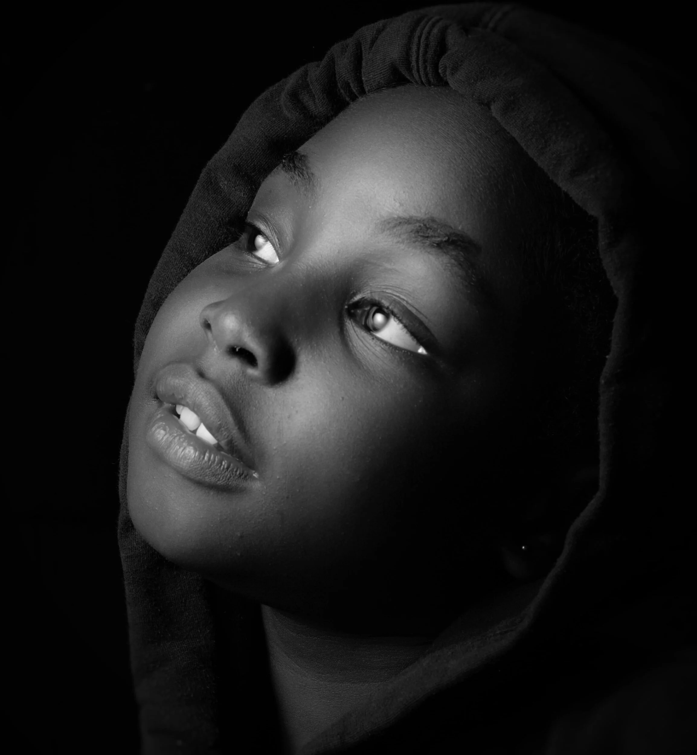 Black and white portrait of a young person with short hair, wearing a hoodie, looking upwards with a contemplative expression.