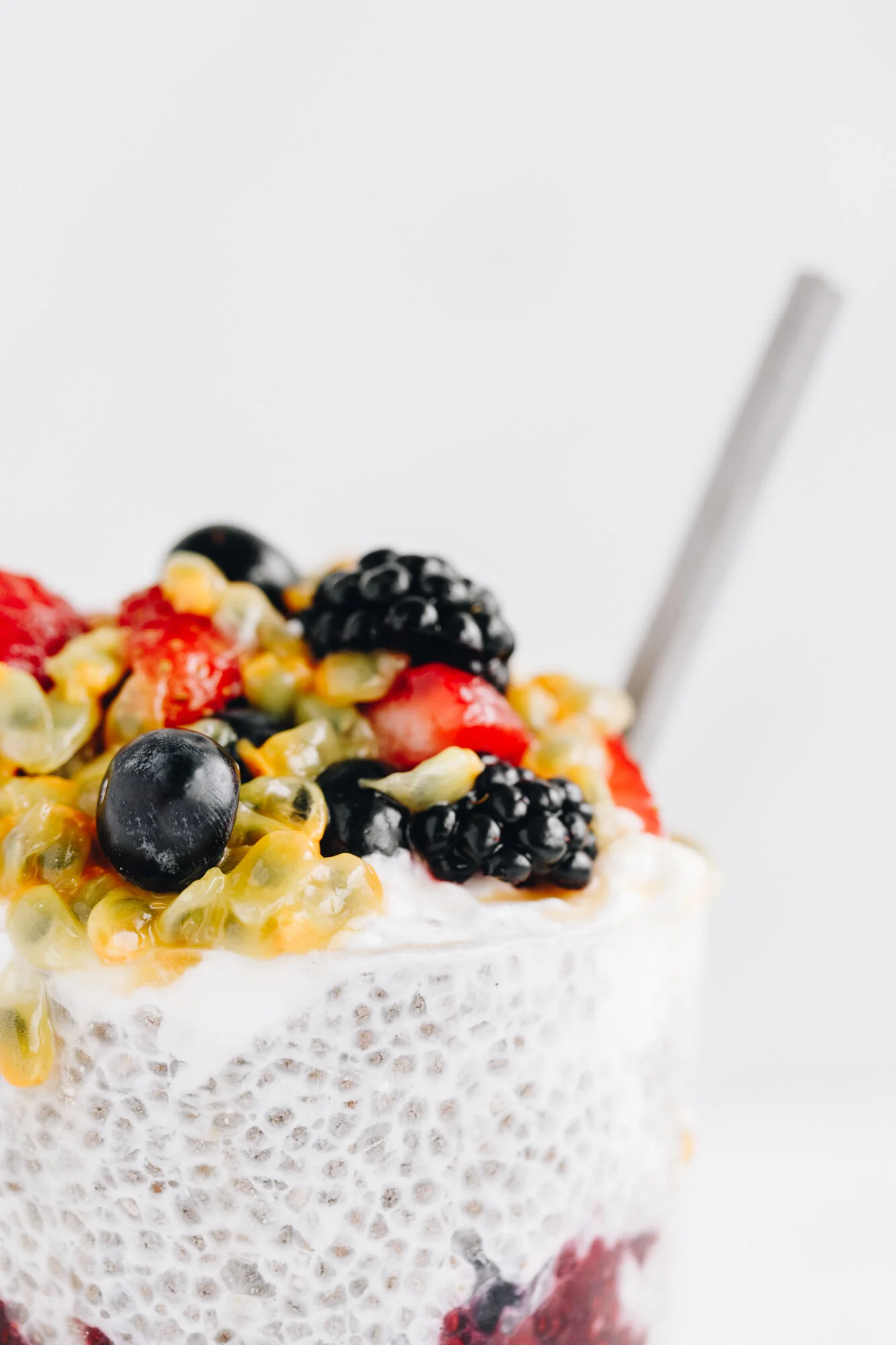 Chia seed pudding topped with assorted berries and passion fruit in a glass, with a metal spoon on the side.