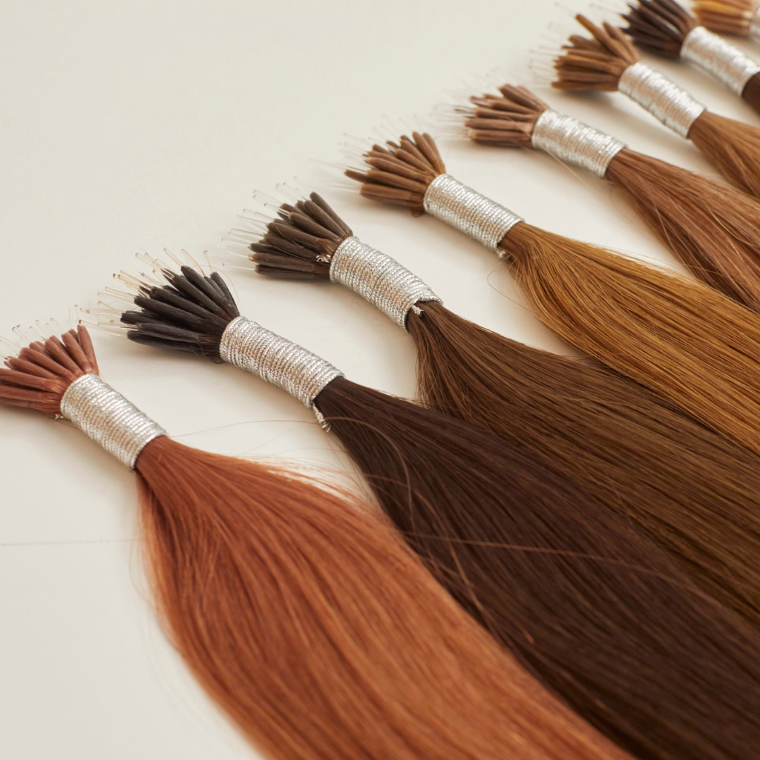 Bundles of colored hair extensions laid out in a row with different shades ranging from dark brown to light brown, wrapped with silver ties.