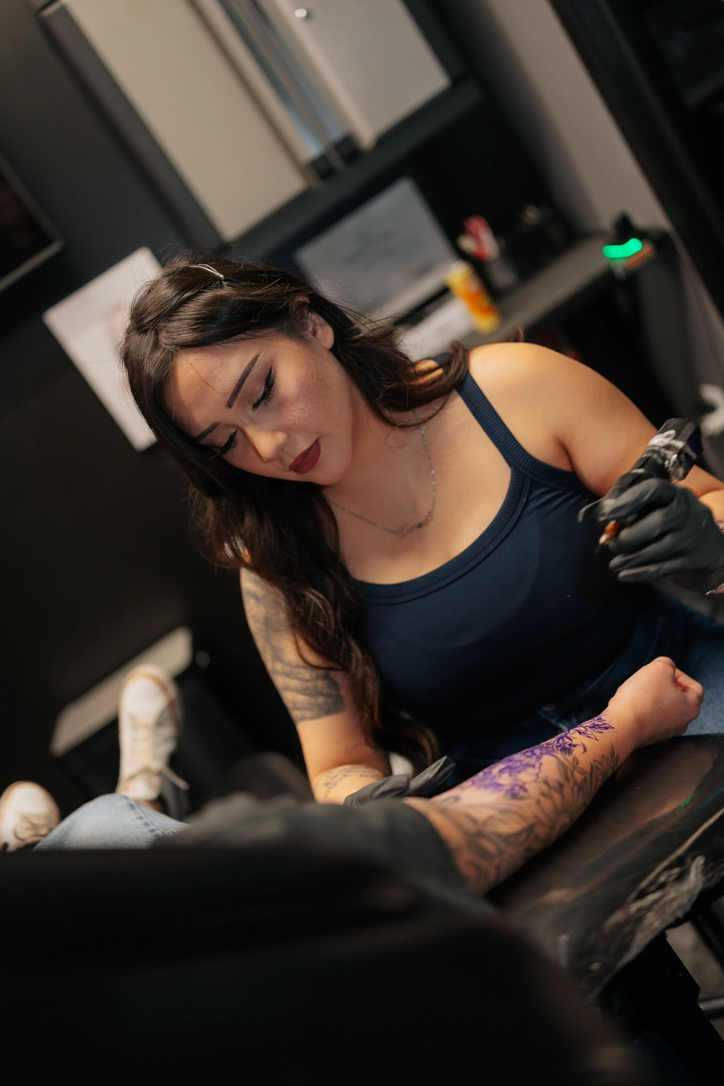 A woman getting a tattoo on her arm in a tattoo parlor.