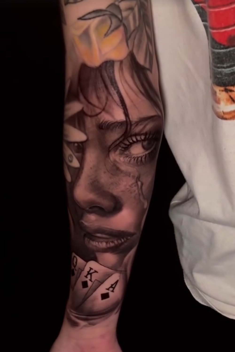 Tattoo sleeve featuring realistic eyes, lips, a leaf, and playing cards on a person's arm.