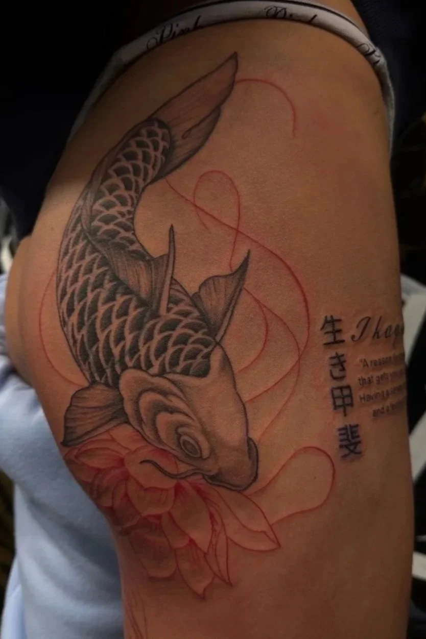 Tattoo of a koi fish swimming around a large flower on a person's upper arm.