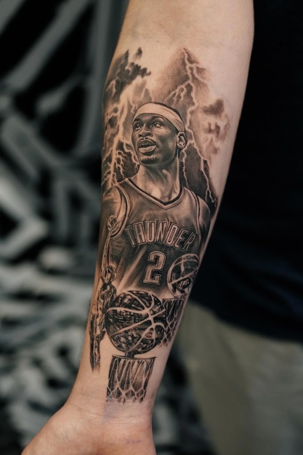 Black and gray tattoo of a basketball player in a Thunder jersey, with lightning and storm clouds in the background, on a person's forearm.