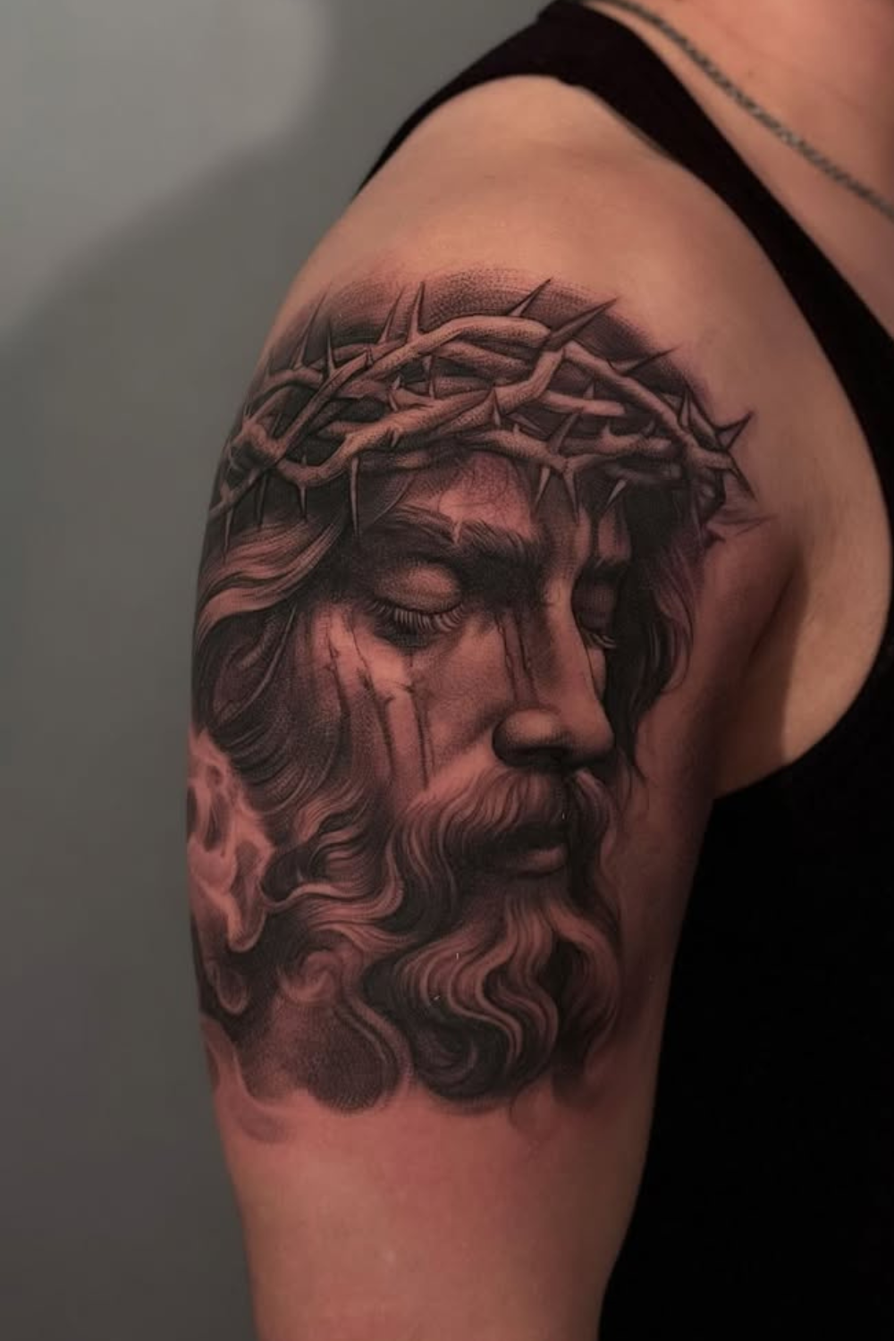 Tattoo of Jesus Christ with a crown of thorns on a person's upper arm