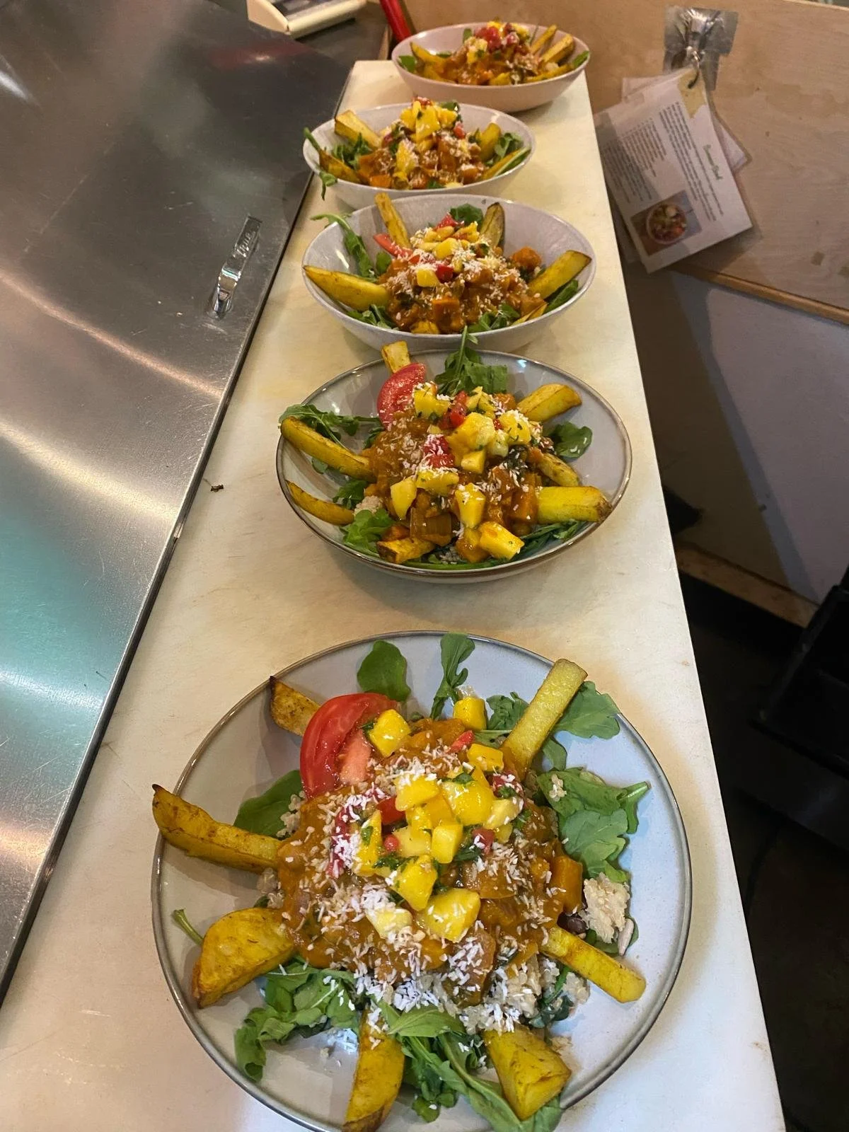 Five bowls of salad with vegetables and roasted fries on a counter.