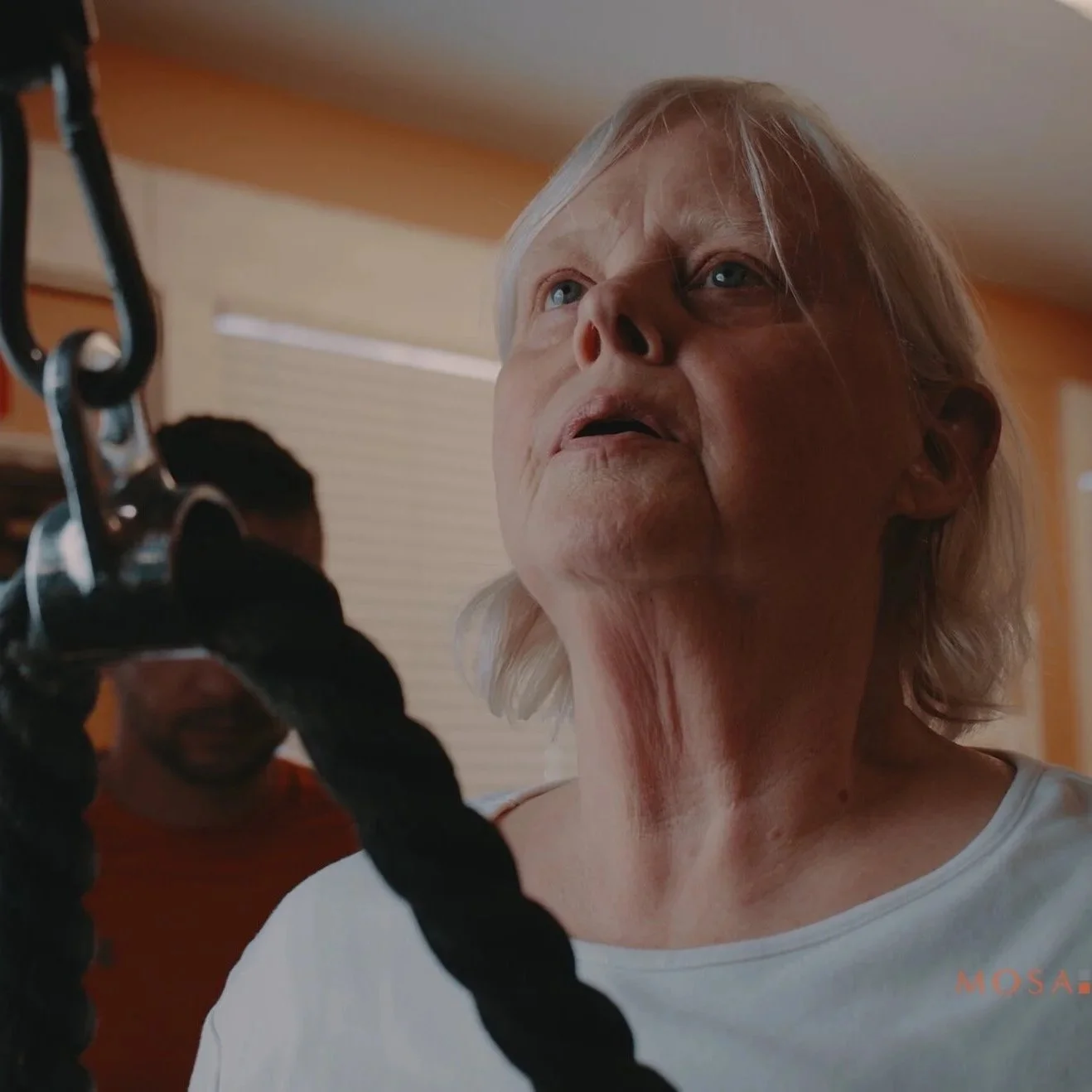 A close-up of an elderly woman with pale skin and white hair, looking upward while working out.