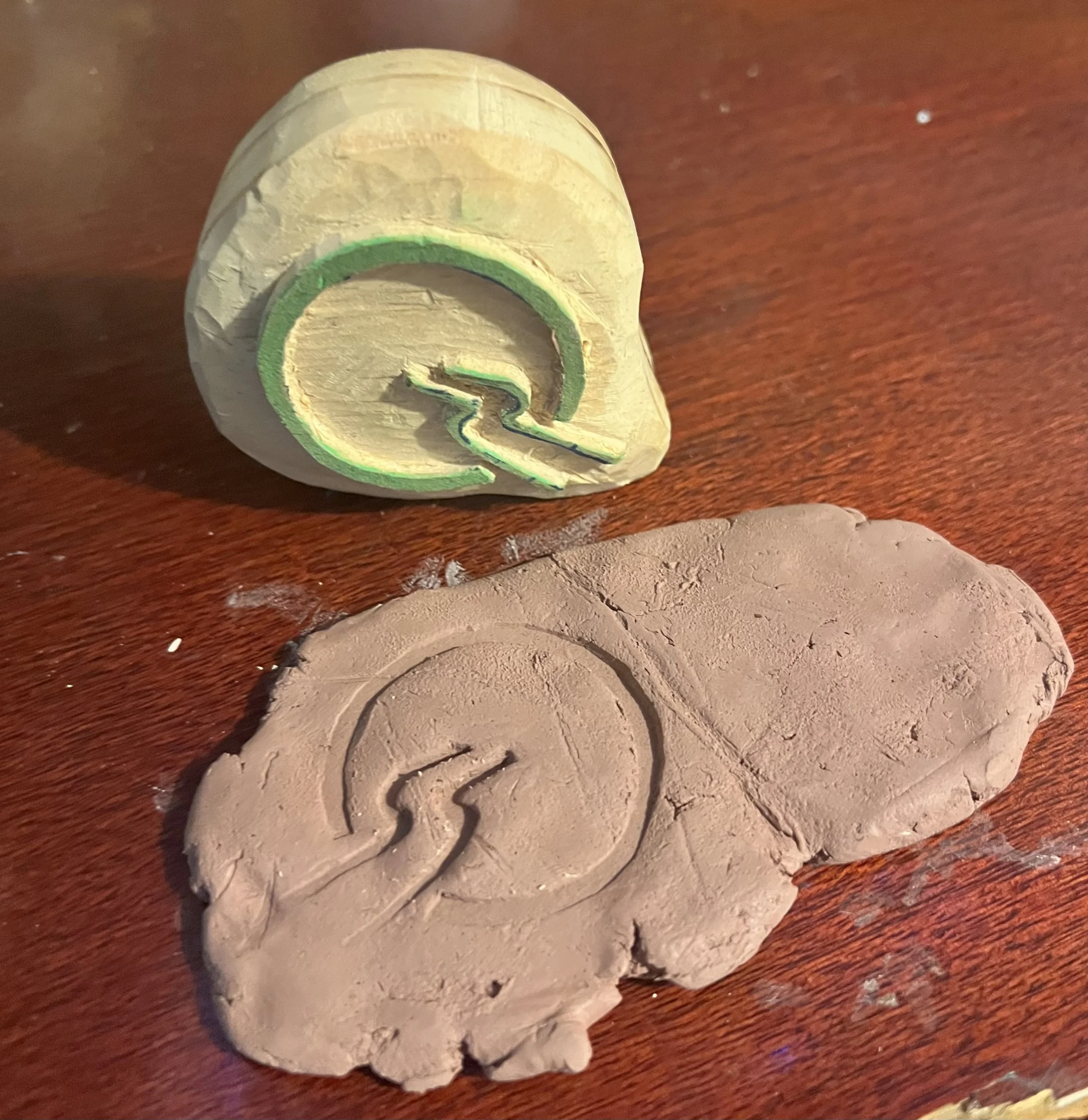 An image of a wooden stamp with the Insightful Path Logo, and a piece of clay on a table which has the impression from the stamp