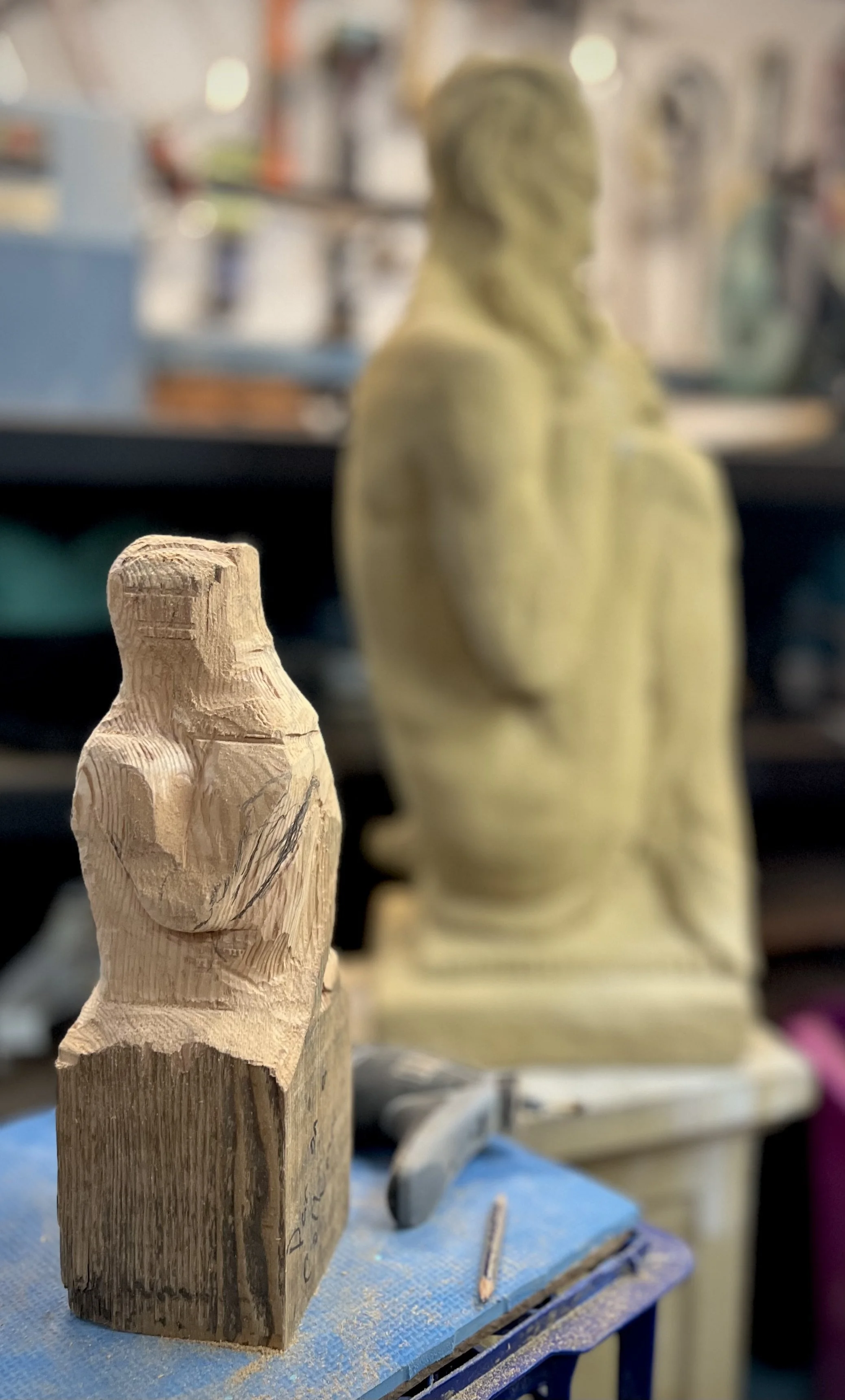 Finished stone Pan sculpture and a partially carved wooden Pan figure placed together inside my woodshed studio.