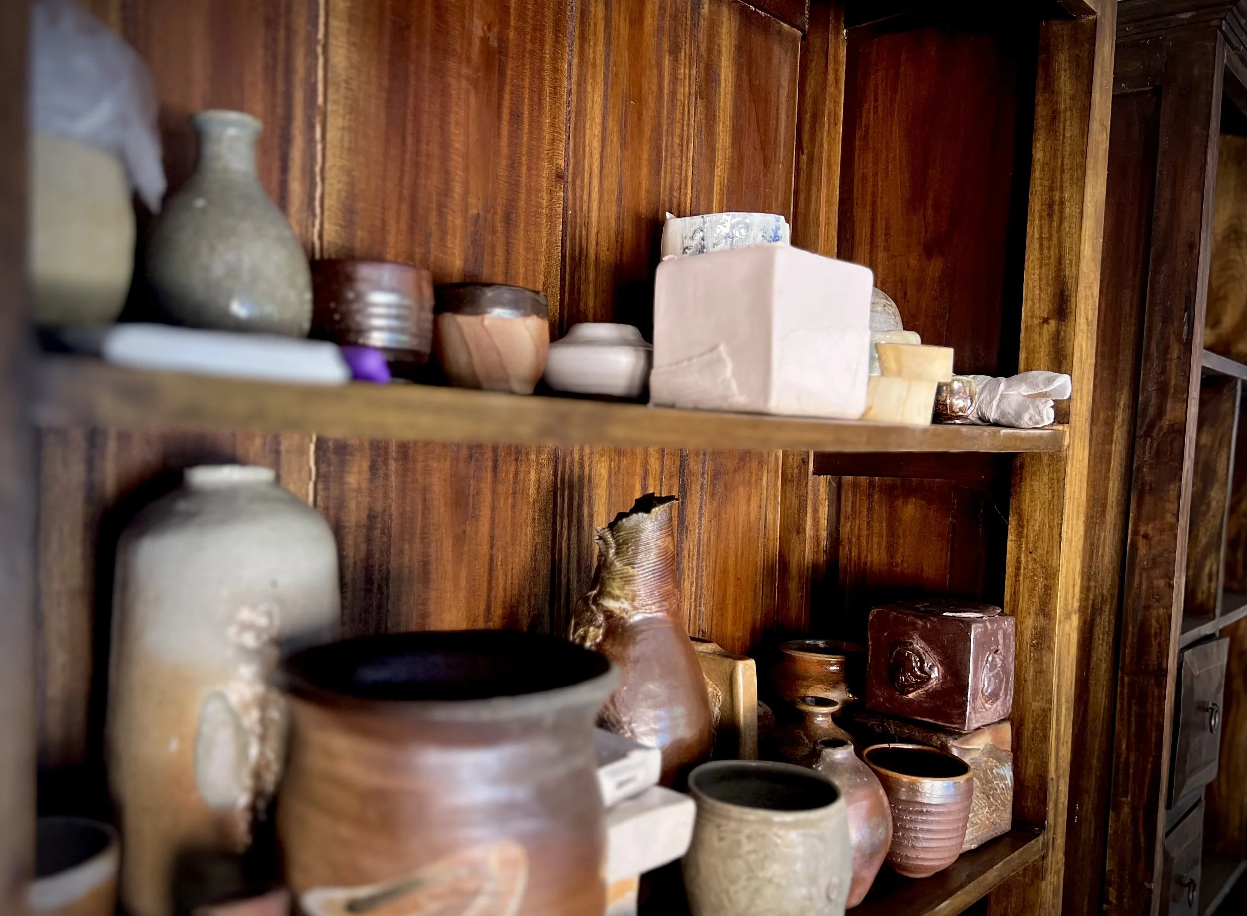 A richly coloured wooden bookshelf filled with pots, cups, and vases hand made by an artist.