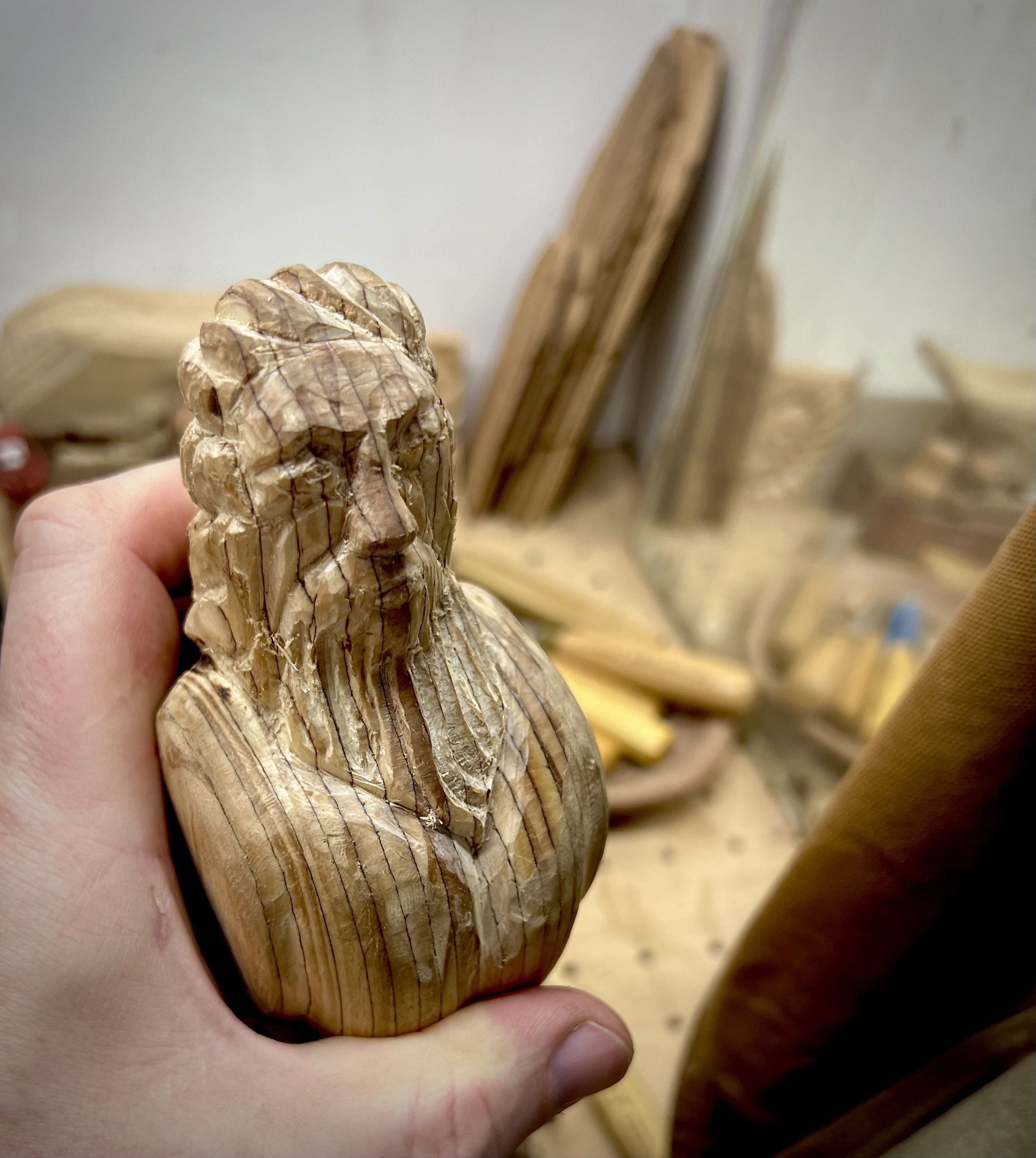 Hand holding an unfinished hand-carved wooden owl with a bearded human-like face.