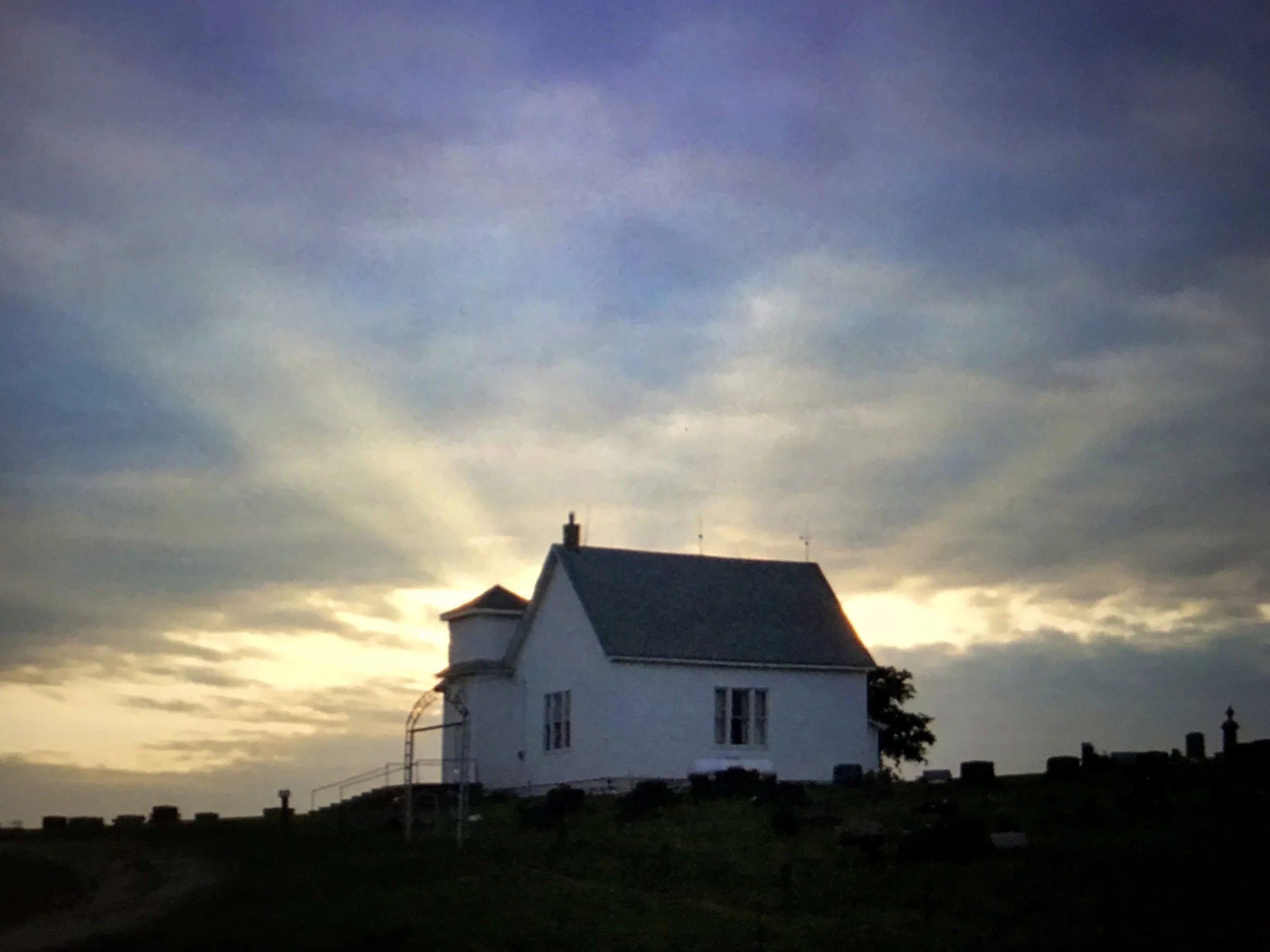 Silhouetted rural church at sunrise after a thunderstorm, with rays of light breaking through dark clouds.
