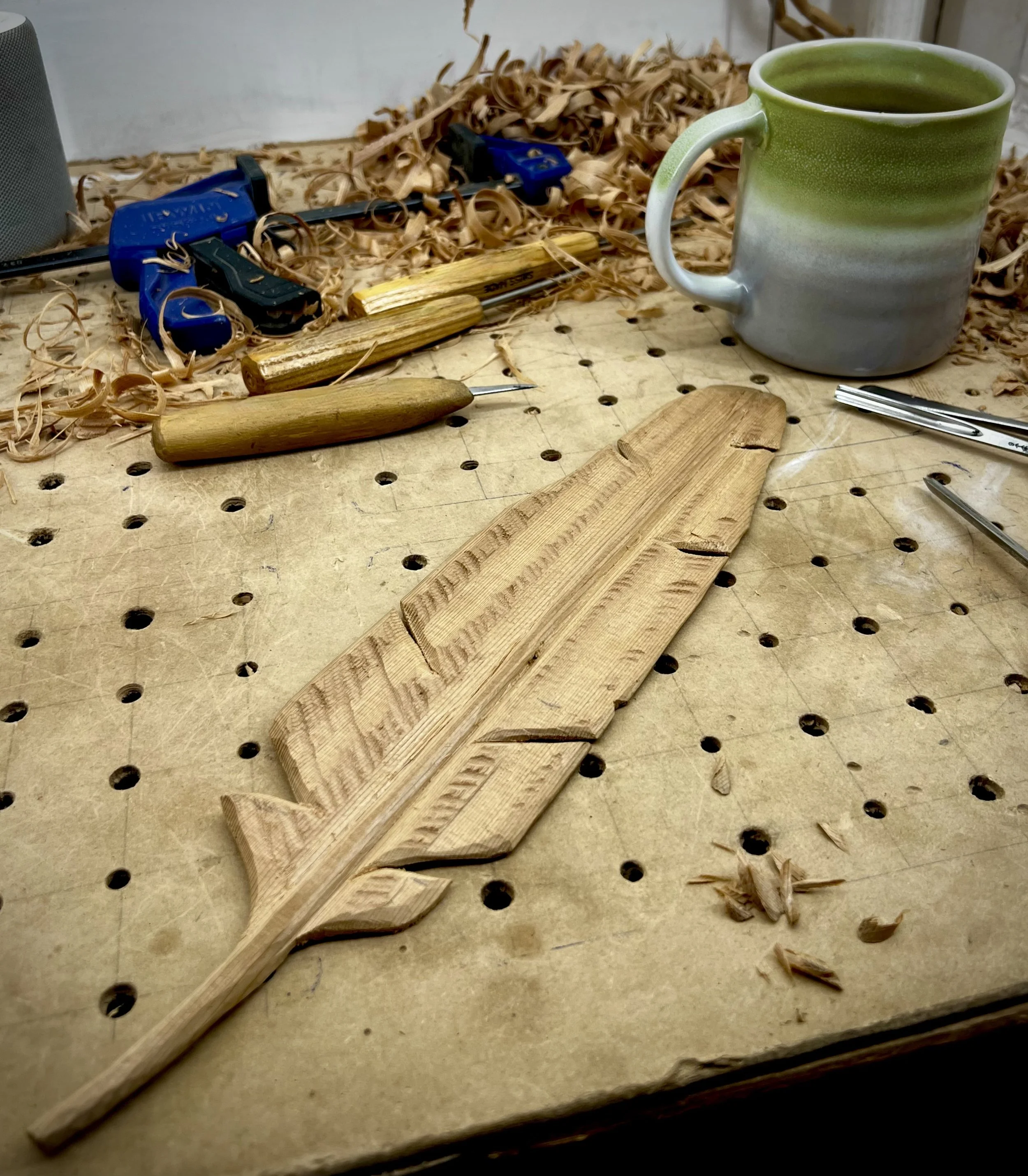 Close-up of a carved wooden feather nearly complete, smooth grain and fine detail visible