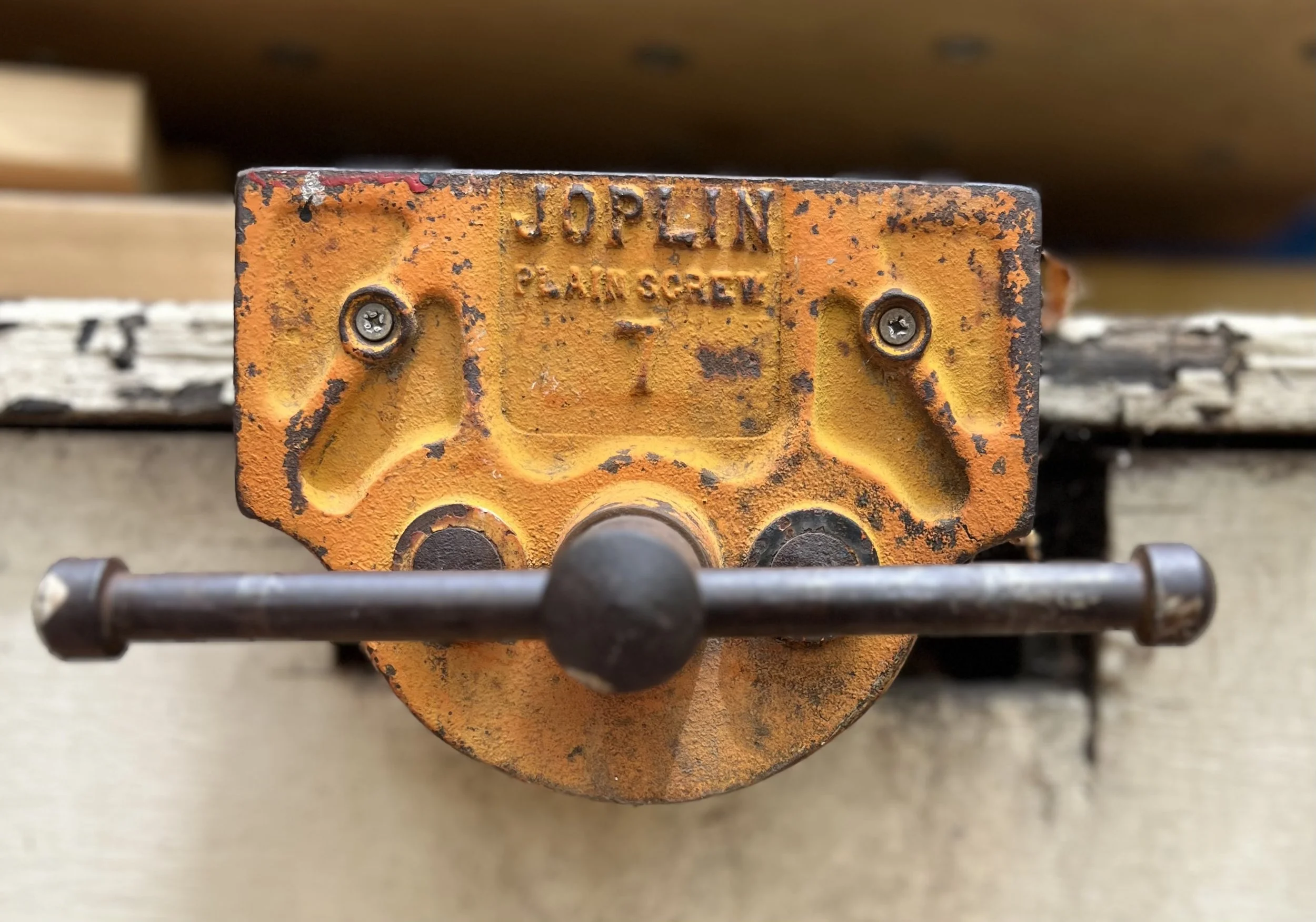 Old cast iron Joplin Plain Screw vice mounted on a workbench, visually resembling a face intently looking at the viewer, through form, and wear.