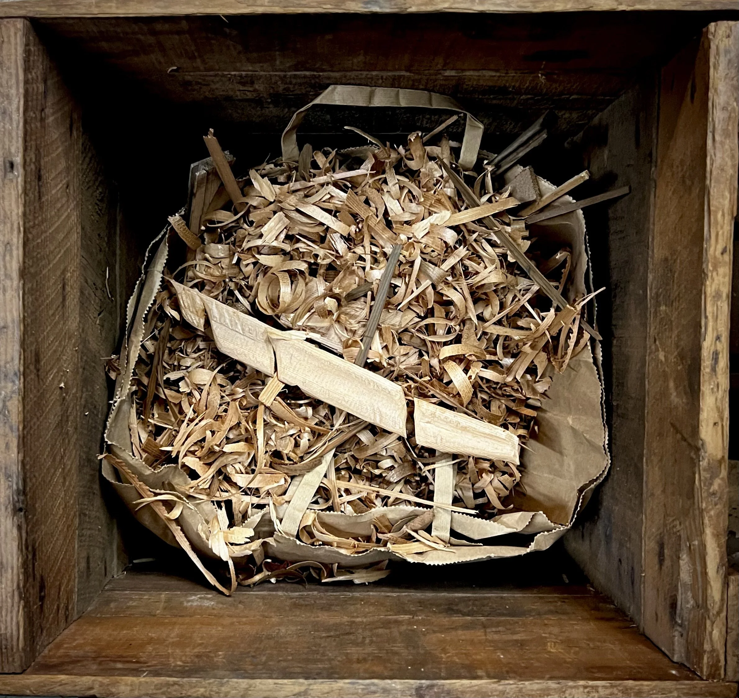Wood shavings and broken feather pieces in a workshop bin, no finished object visible