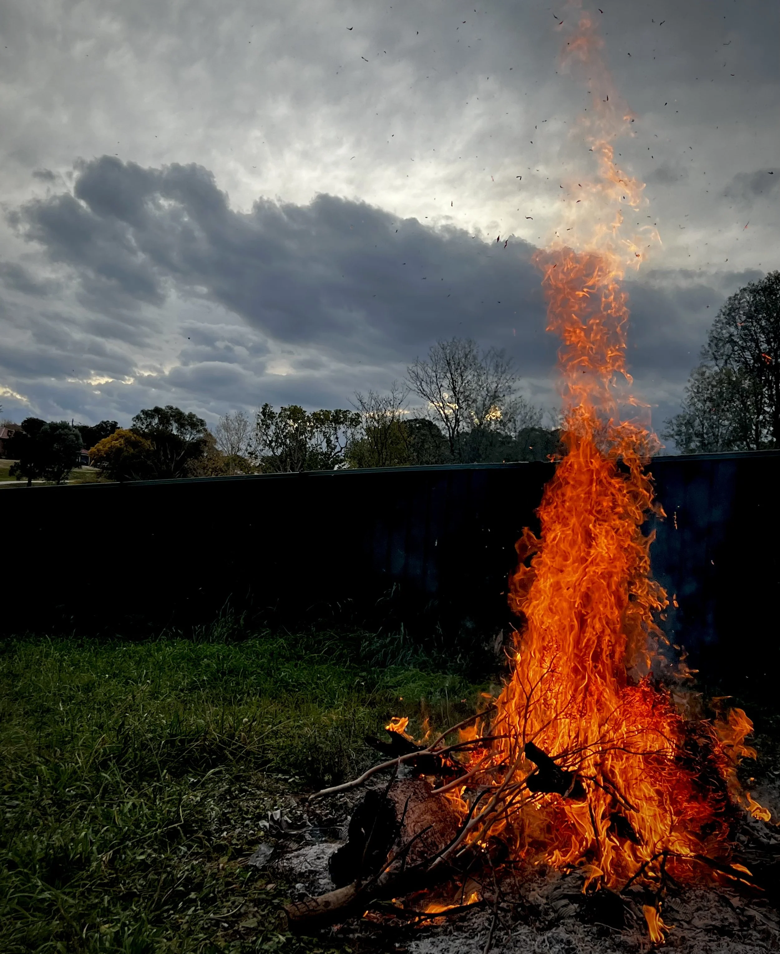 Fire rising into the evening with dark clouds overhead and fading sunlight