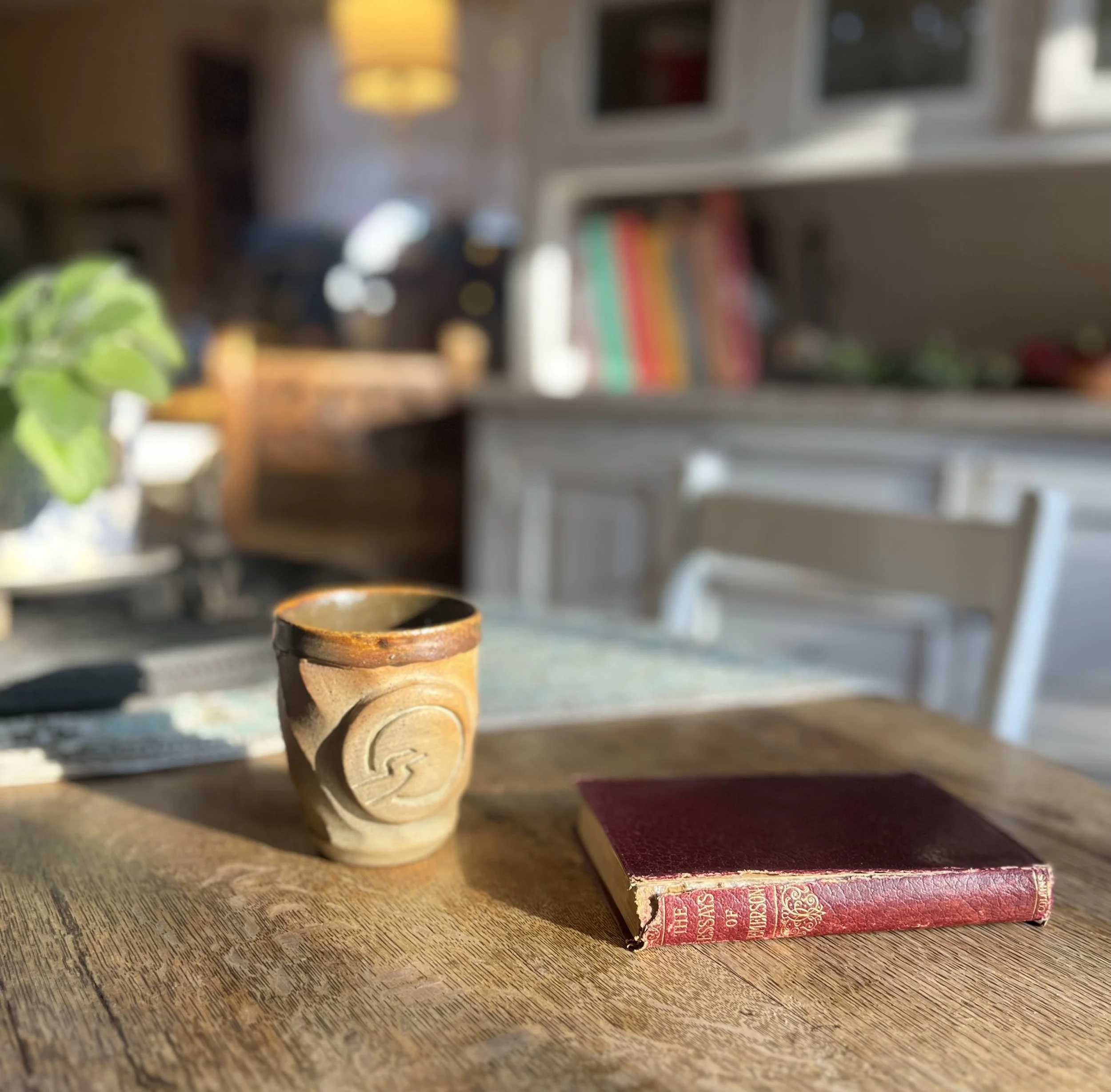 Red leather bound Emerson essays on a sunlight wooden table beside a cup of tea with Insightful Path logo