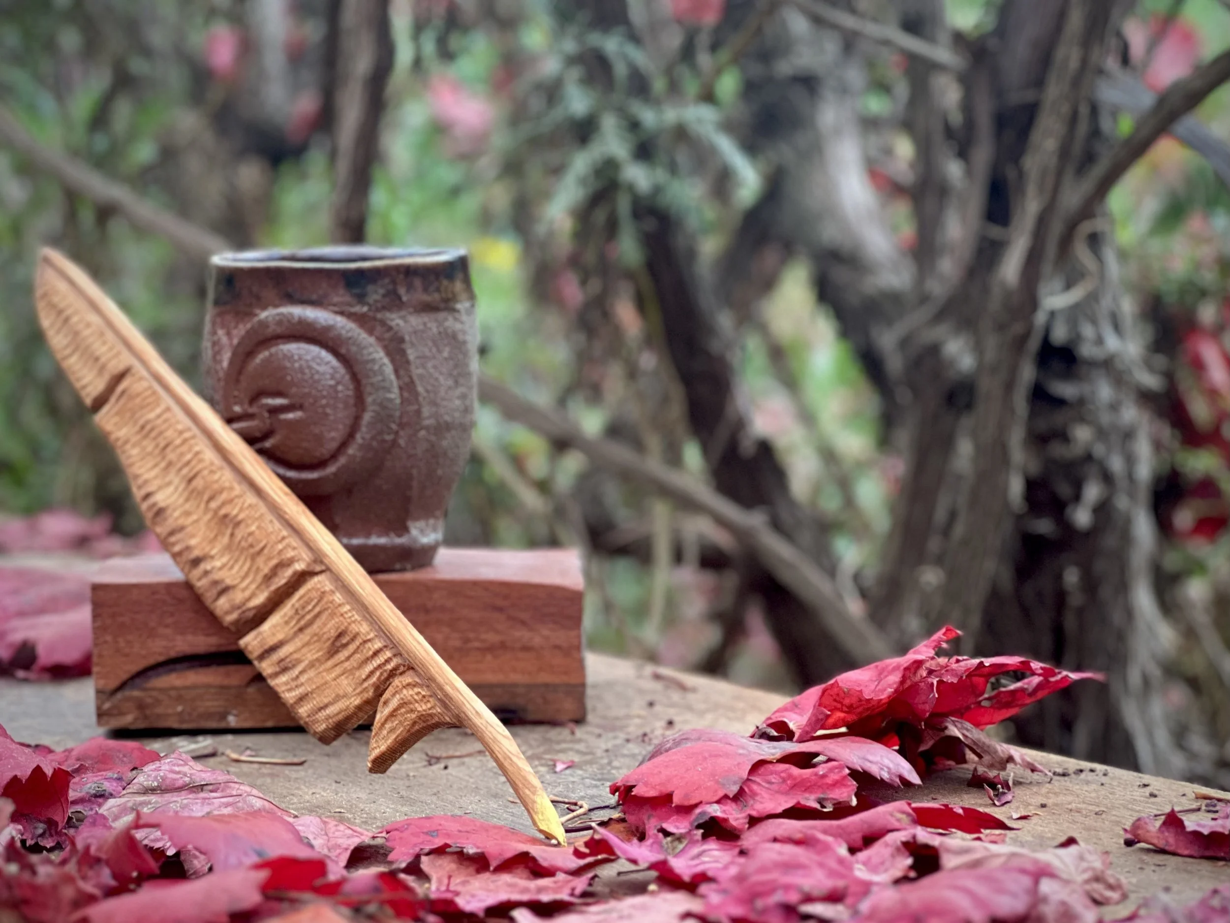 Finished wooden quill resting against polished red gum slab, surrounded by red leaves and tea cup