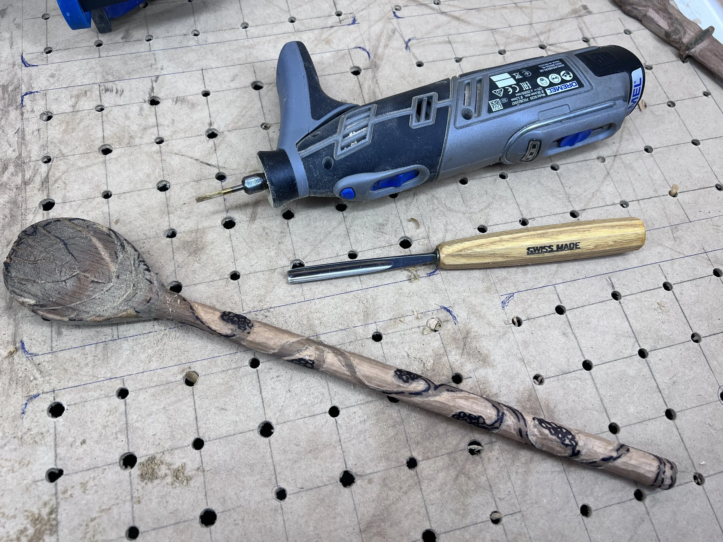 Hand tools and power tools arranged together on a workbench with a wooden spoon, mid process of being made.