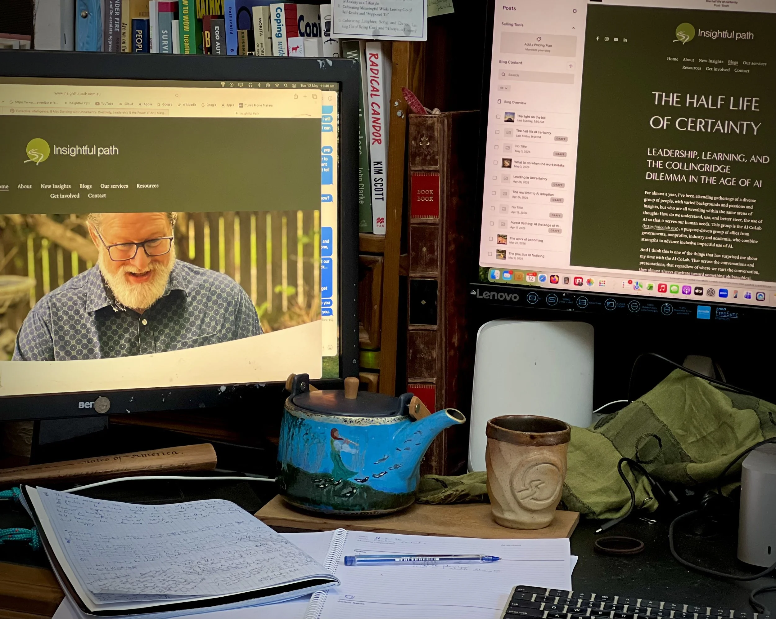 A desk covered in annotated books, and handwritten notes, beside a modern computer displaying text and website design.
