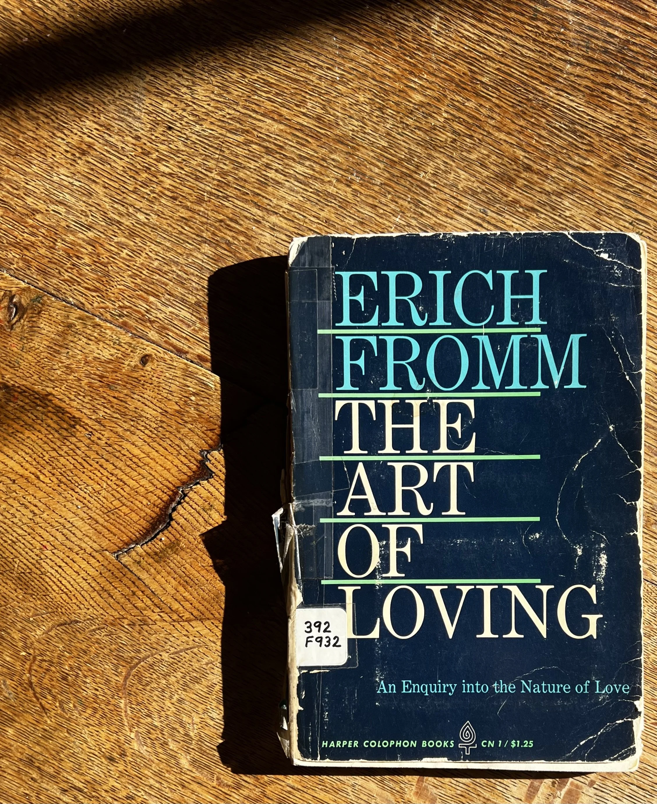 Dog-eared copy of Erich Fromm’s The Art of Loving resting on a wooden table with worn pages visible.