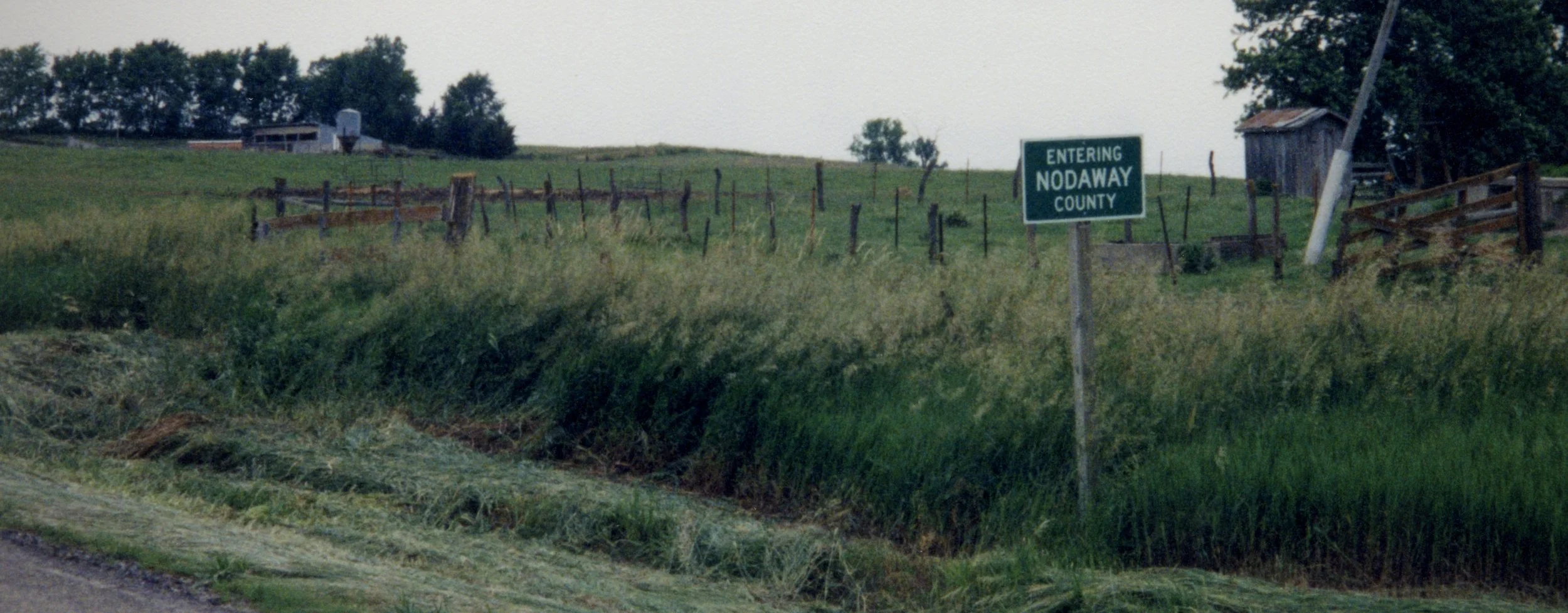 Roadside sign reading “Entering Nodaway County” beside tall grass and farmland in rural Missouri.