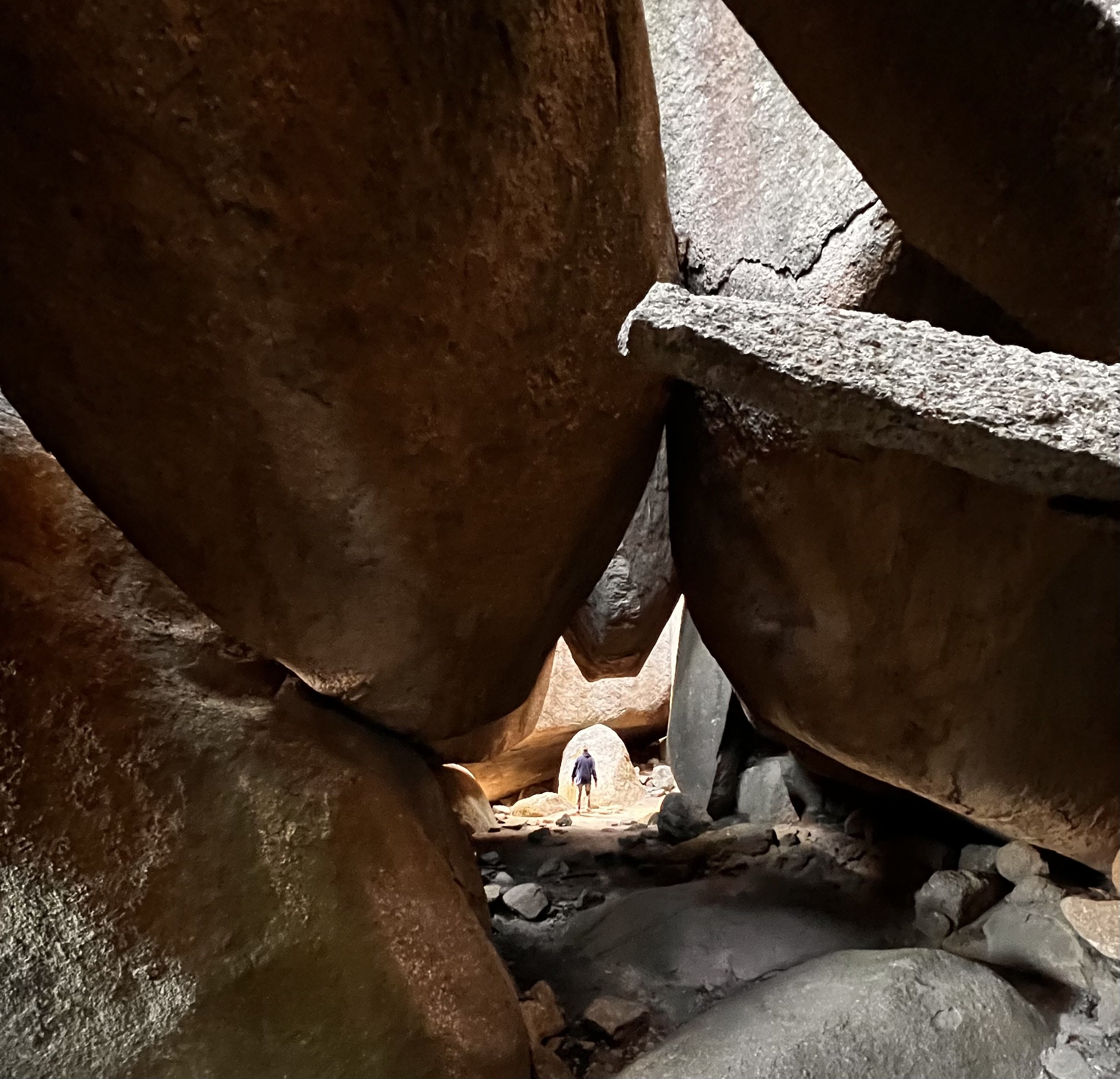 A vast cave interior with shafts of light on rock walls; a small climber stands with their back to the camera, emphasising scale, humility, and exploration.