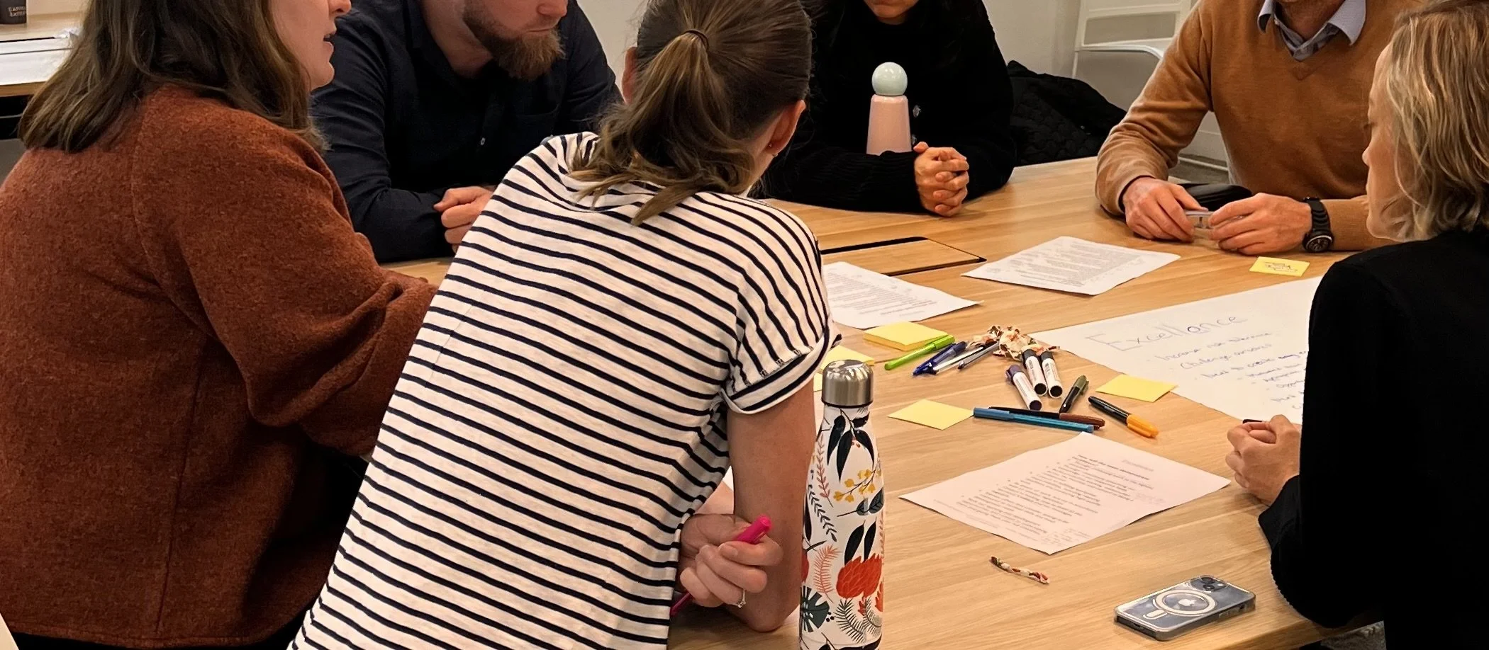 A group of professionals engaged in a facilitated discussion or workshop setting, arranged in a circle, with visible engagement and shared attention rather than hierarchical presentation.