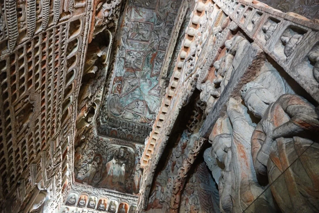 Intricate stone carvings and frescoes on a high, arched ceiling of a historic temple or monument.