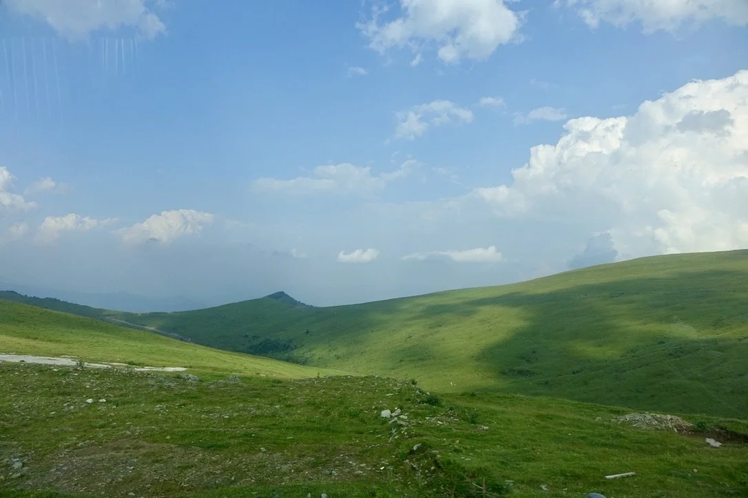 Green rolling hills under a partly cloudy blue sky in a rural landscape.