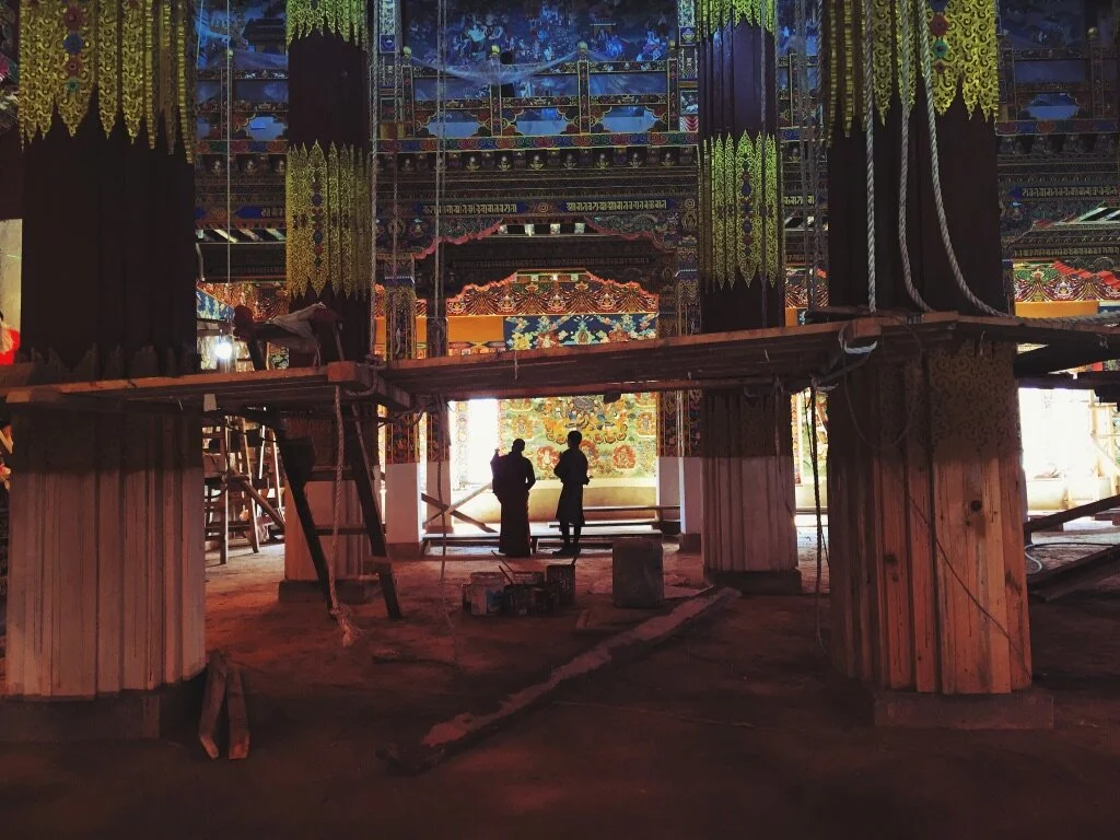 People working under a decorated, colorful stage or altar with intricate patterns, likely in a cultural or traditional setting, possibly a temple.