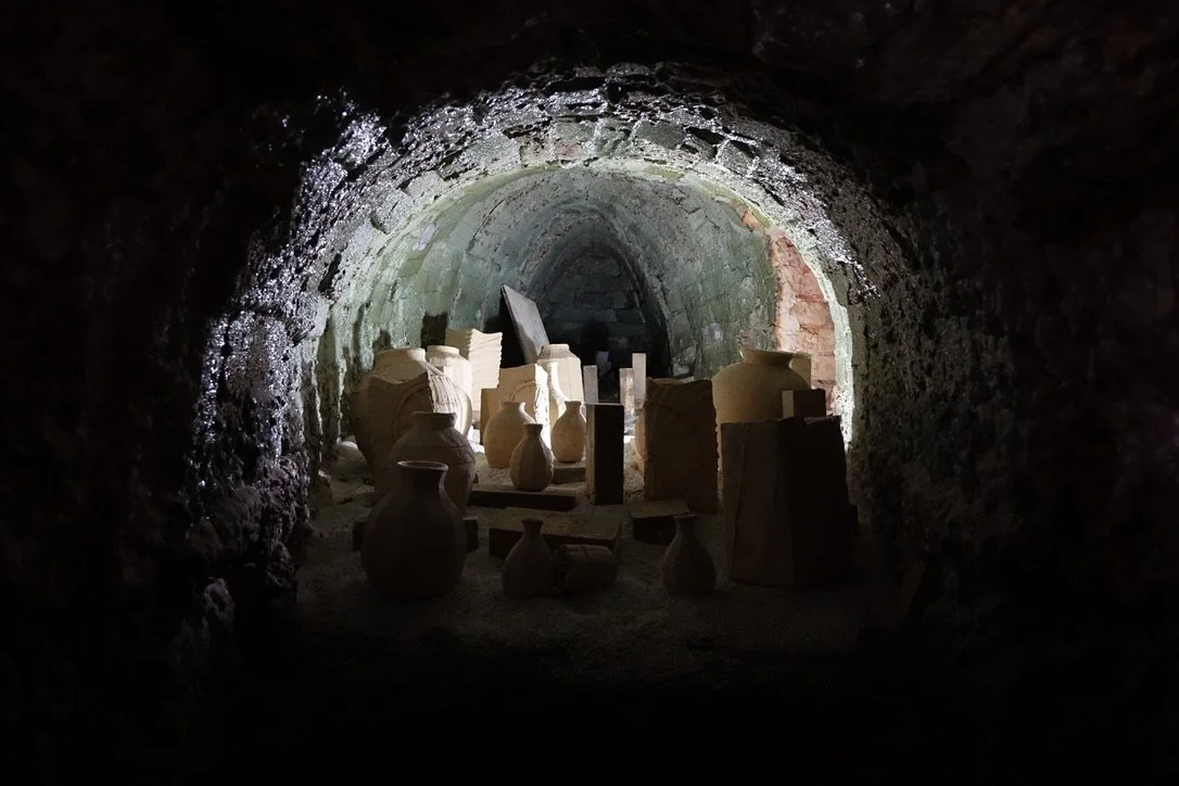 Underground archaeological site with ancient pottery and artifacts illuminated by dim light.