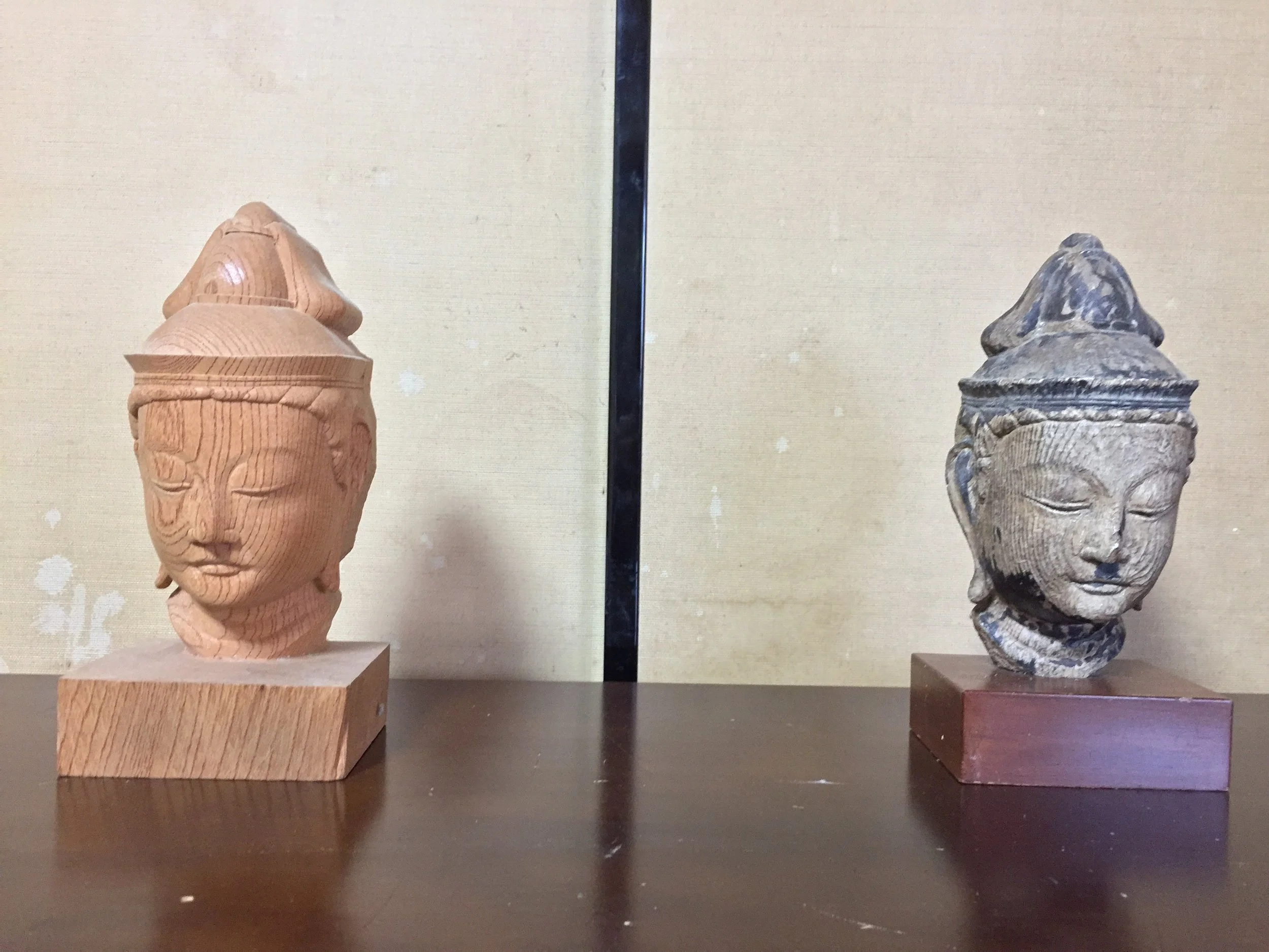 Two carved sculptural heads displayed side by side on wooden bases against a neutral wall.