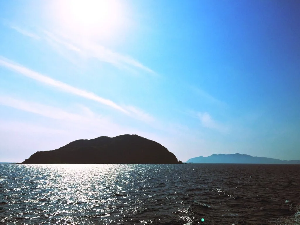 Ocean with a large island and distant landmass under a partly cloudy sky.
